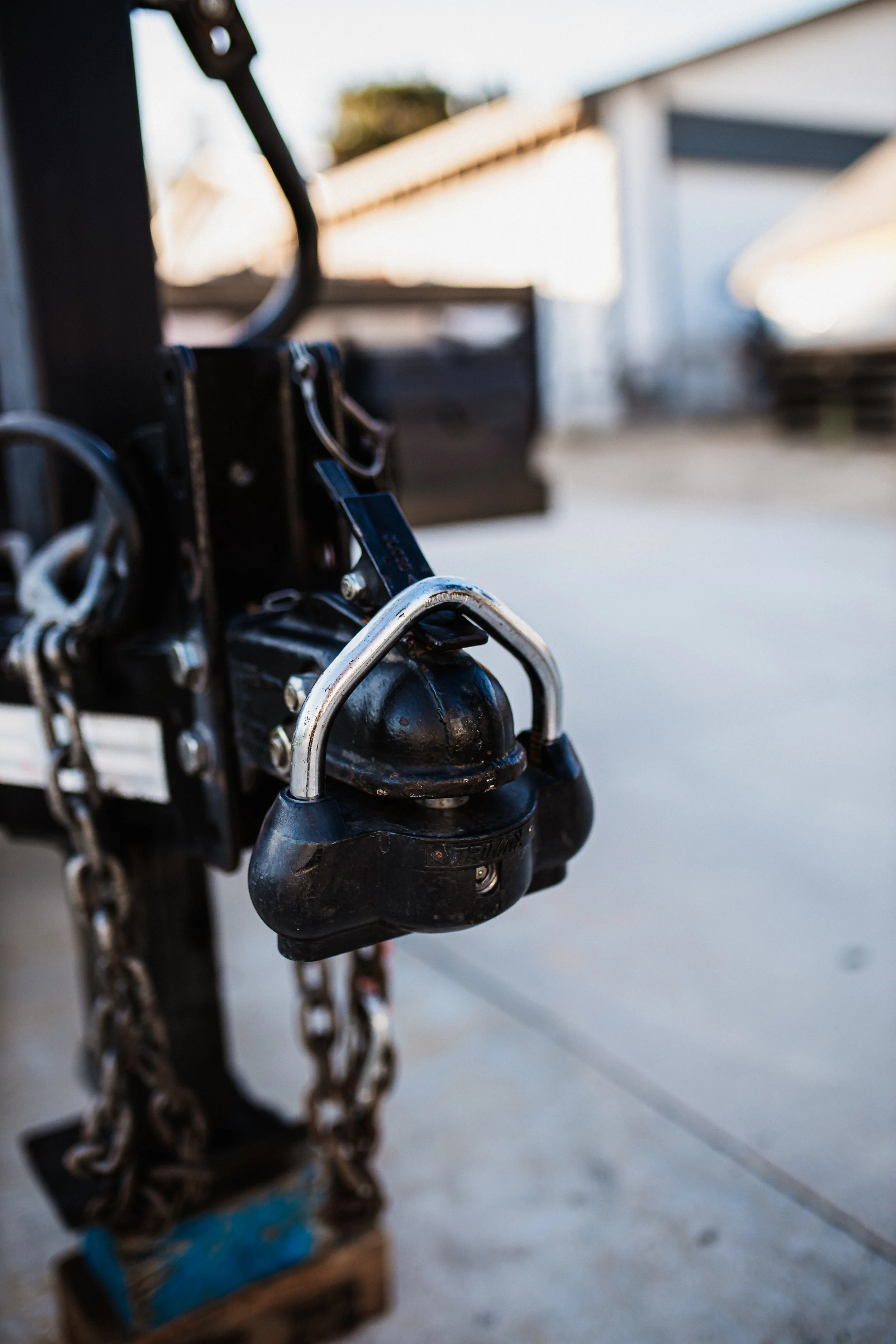 Close-up of a trailer hitch lock secured with a chain, attached to a trailer parked outdoors.