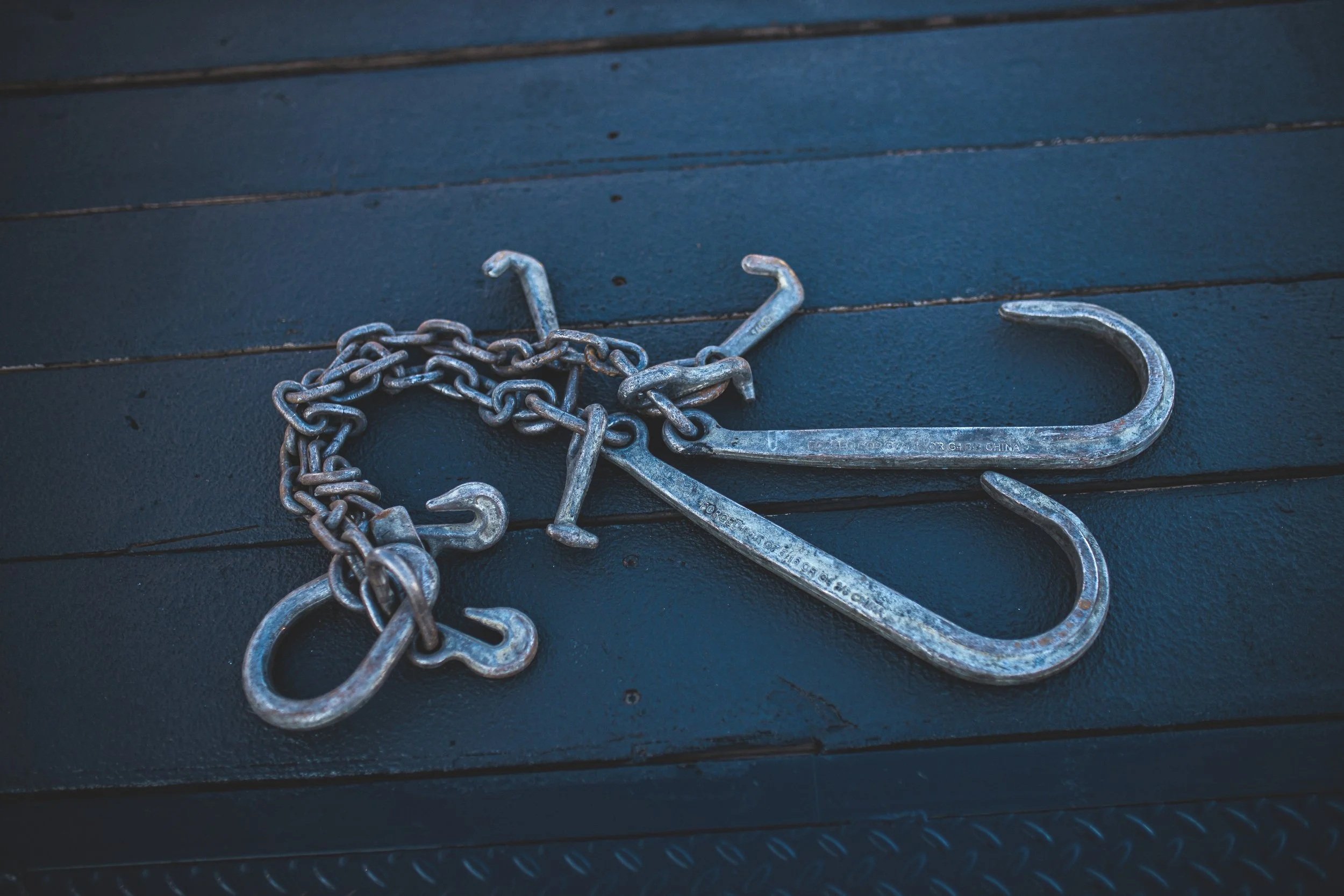 A large metal hook, two smaller hooks, and a chain lying on a dark blue surface.
