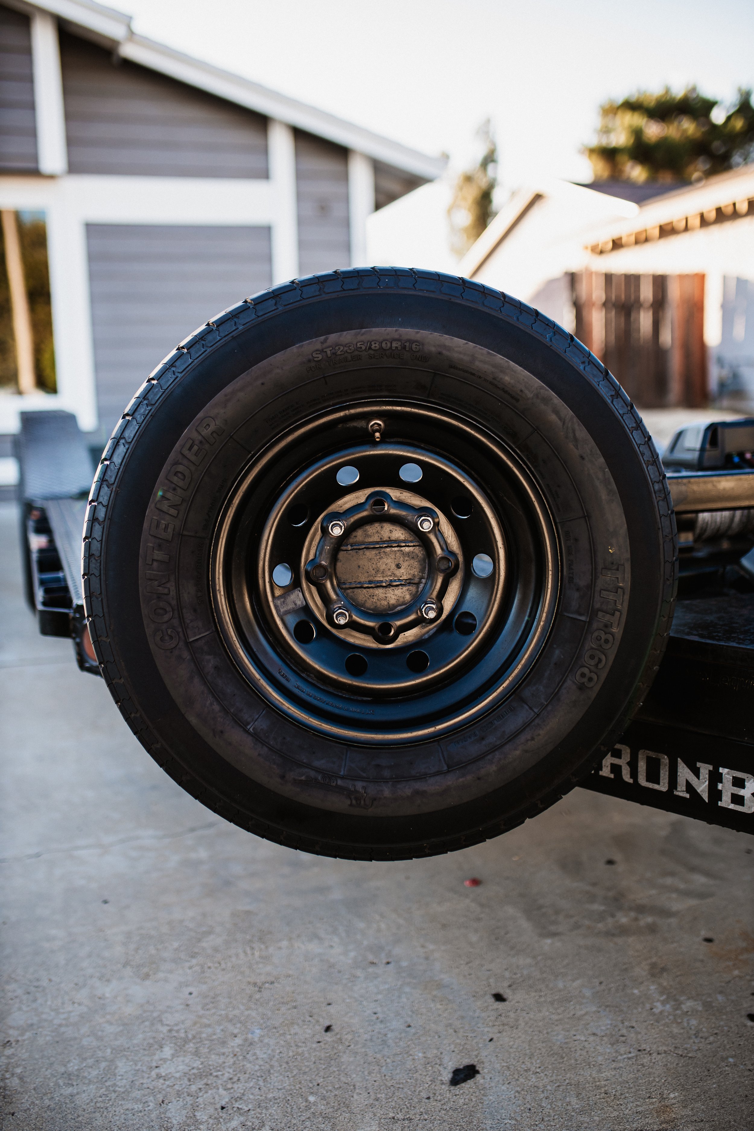 Close-up of a spare tire mounted on a vehicle, with a house and a backyard in the background.