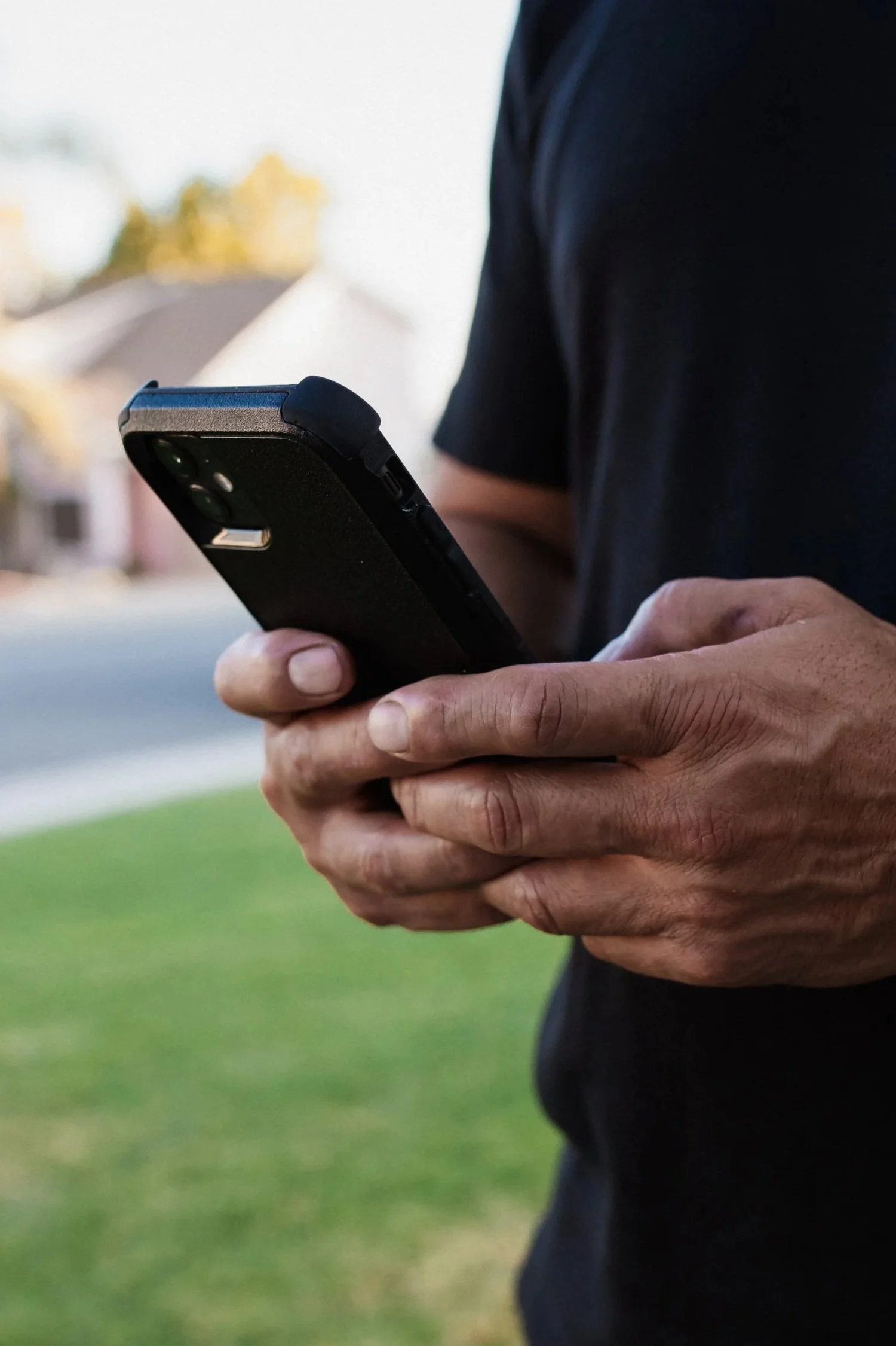 A person holding a smartphone outdoors on a sunny day.