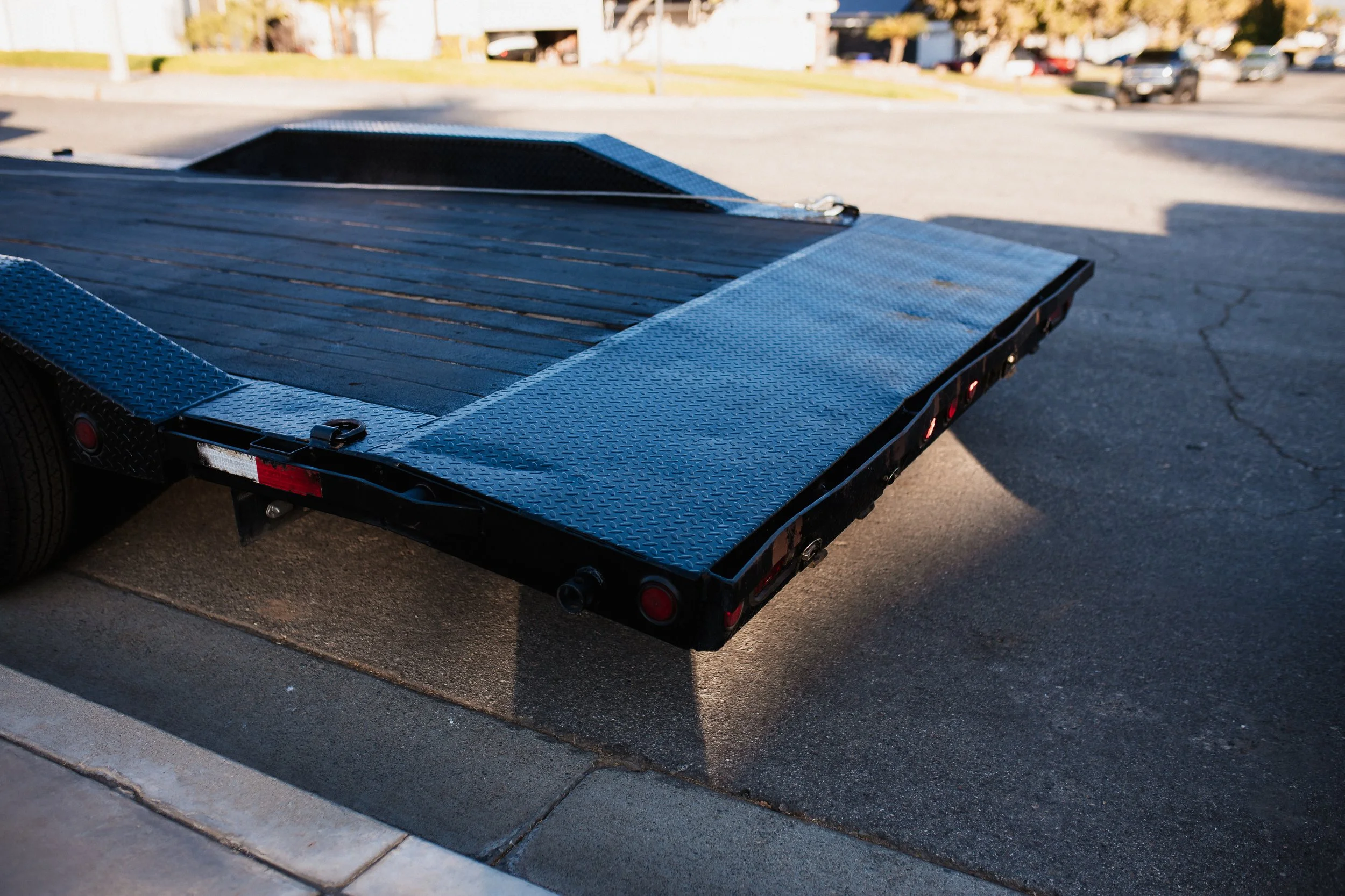 Black flatbed trailer parked on a street with a residential area in the background.