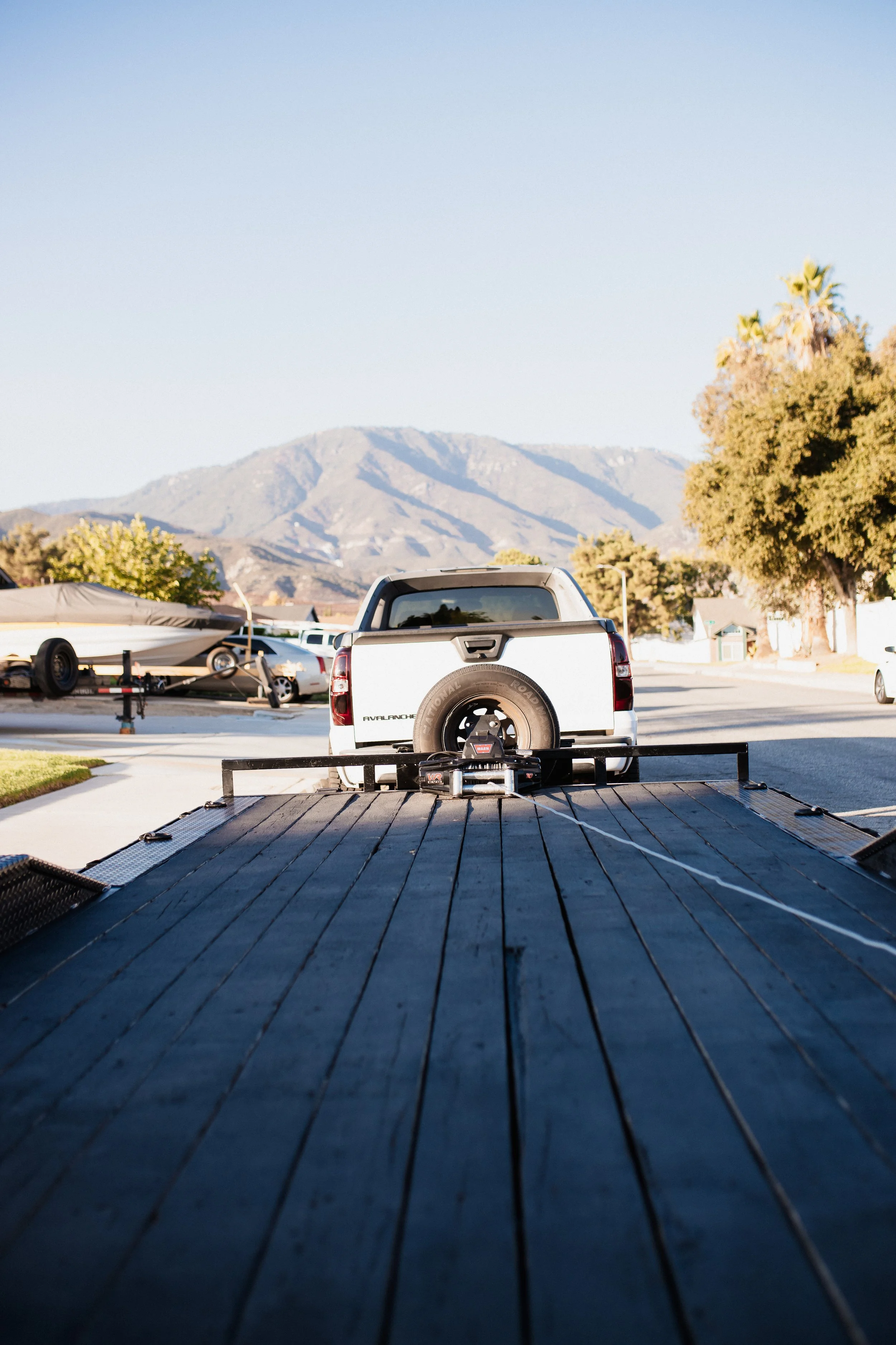 A truck on a flatbed trailer, seen from the back, parked on a residential street with mountains in the background.