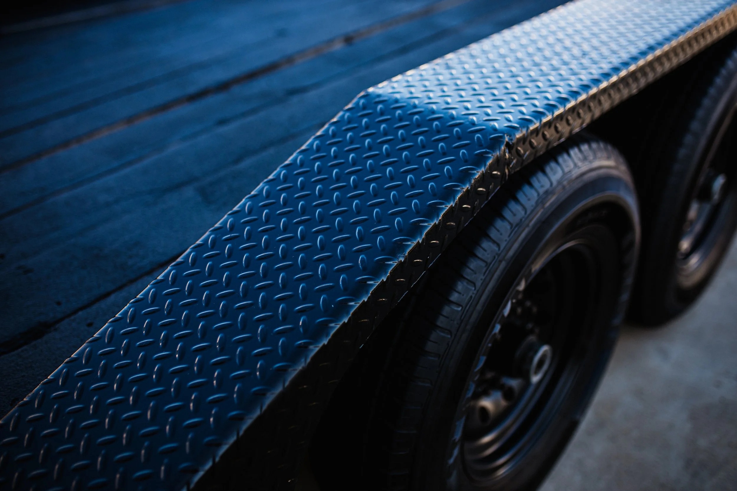 Close-up of a black trailer with metal diamond plate on the edge and black tires underneath.