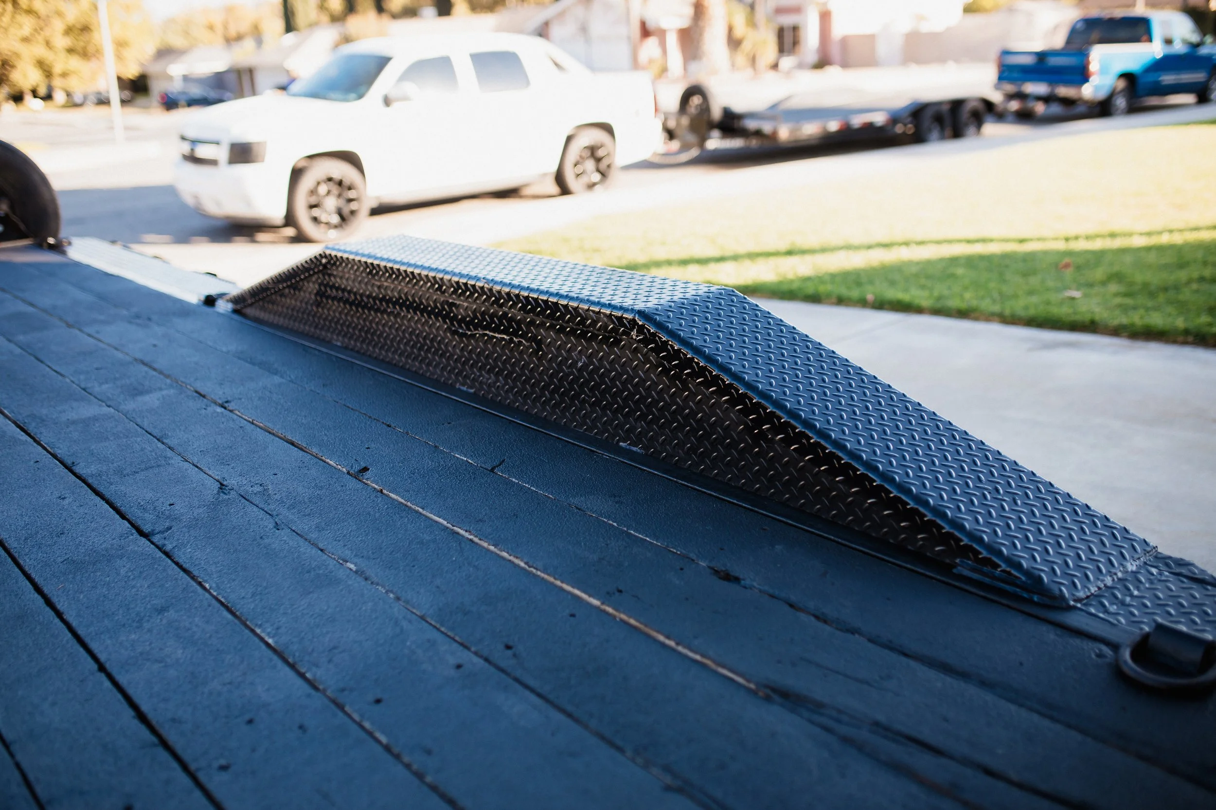 Close-up view of a black metal ramp on a trailer, with a street and parked cars in the background.