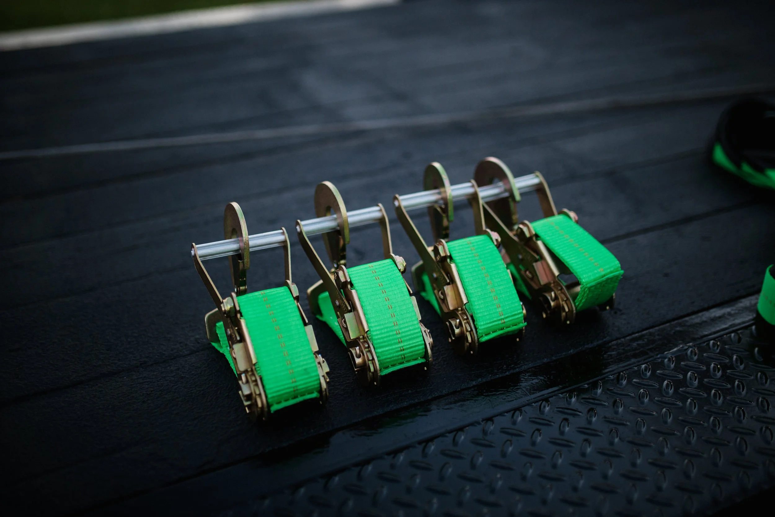 A set of four green and metal climbing harnesses placed on a black rubber gym floor.