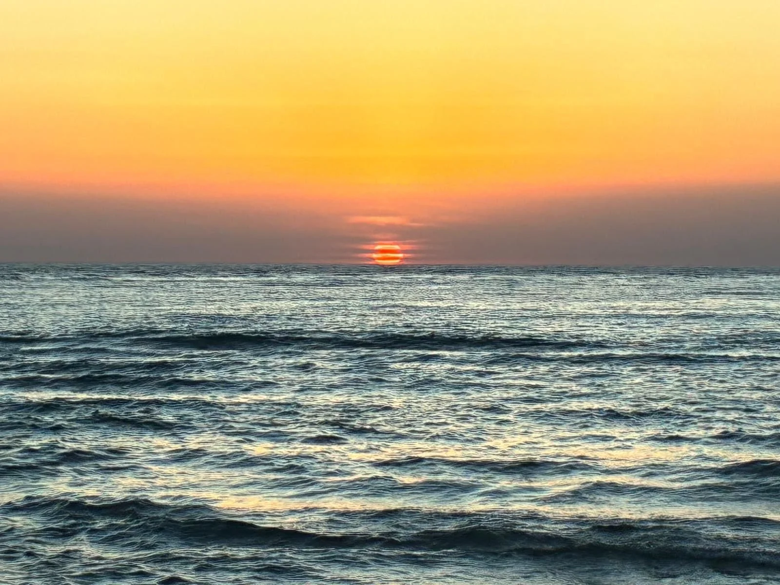 Zonsondergang boven zee, met de zon laag aan de horizon en zacht golvend water op de voorgrond.