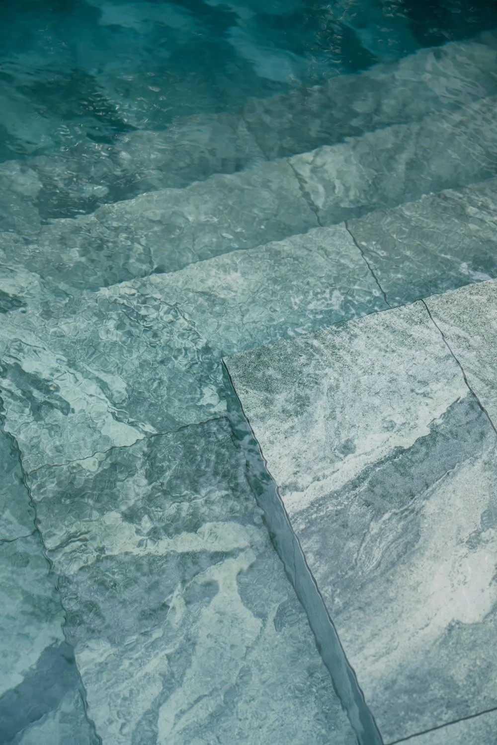 Close-up detail of submerged natural stone steps inside a luxury villa swimming pool, showing the texture and veining of the stone through clear water, designed by Limestone in Dubai