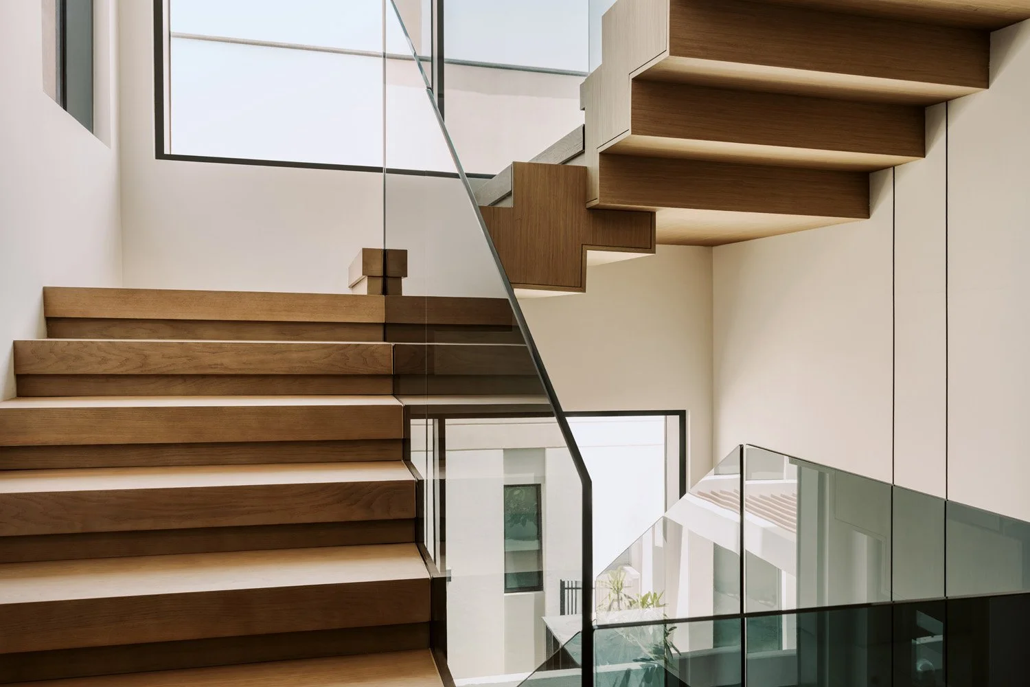 Dramatic floating staircase with cantilevered oak treads, full-height glass balustrade, and double-volume void designed by Limestone