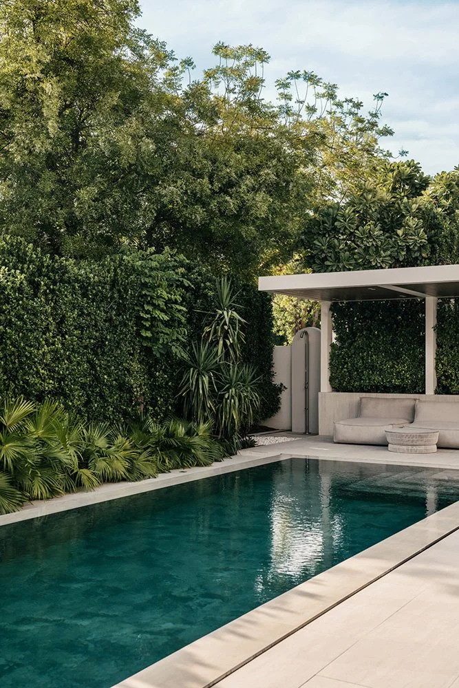 Luxury villa pool with a minimalist white canopy structure, built-in lounge seating, dense tropical garden screening, and stone pool coping, designed by Limestone in Arabian Ranches Dubai