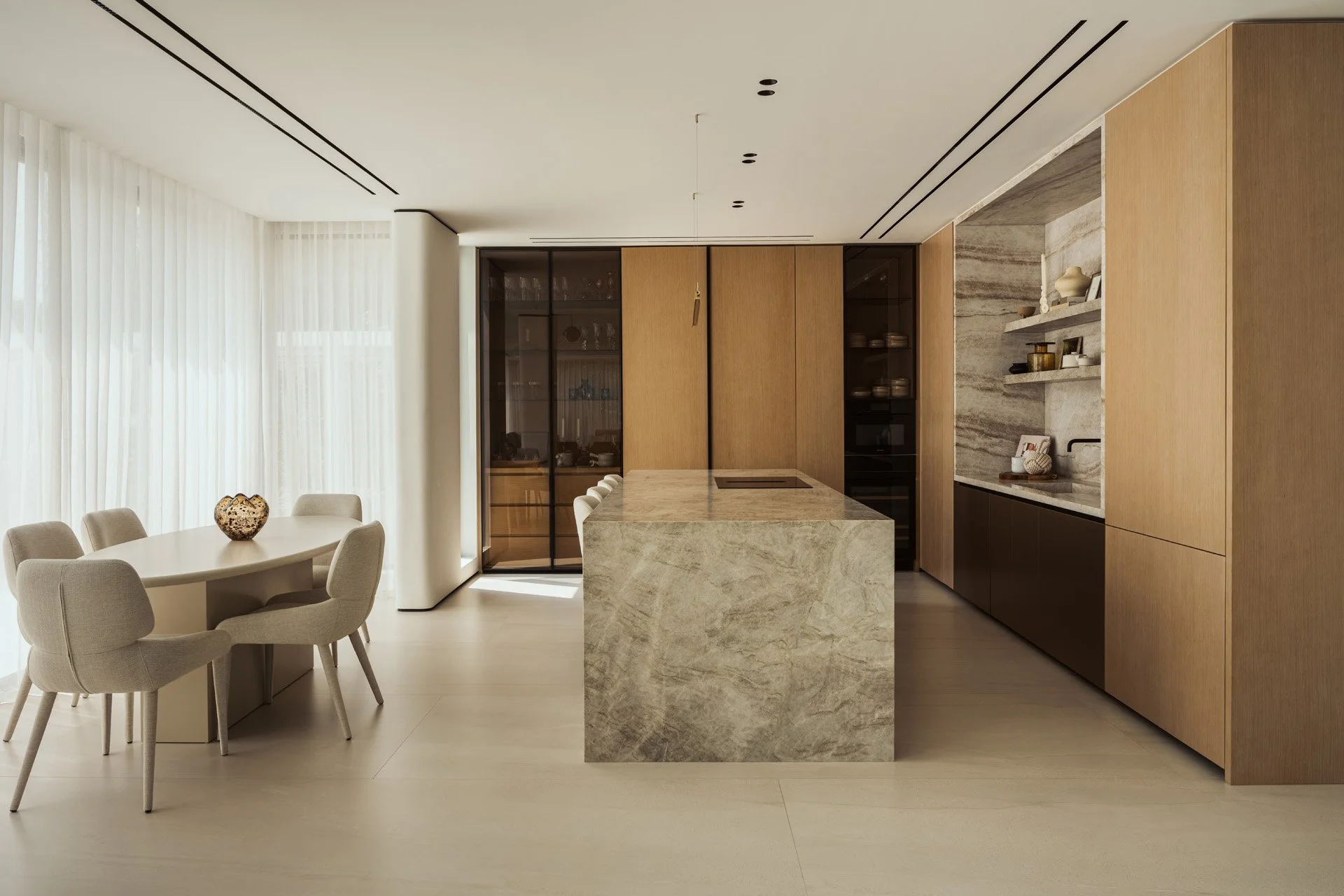 Open kitchen in Villa Ambra, a Jumeirah Islands villa renovation by Limestone, with a Taj Mahal quartzite island, oak joinery, glass-fronted cabinets and an oval breakfast table.