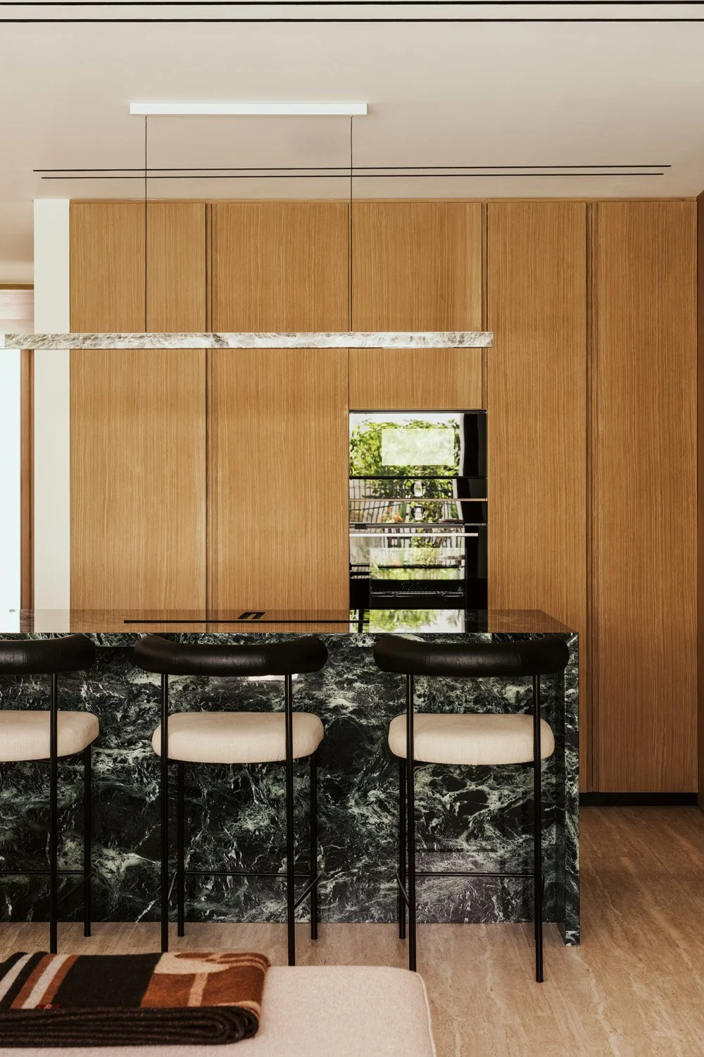 Luxury kitchen design featuring a dramatic green marble island with leather bar stools and floor-to-ceiling oak cabinetry by Limestone