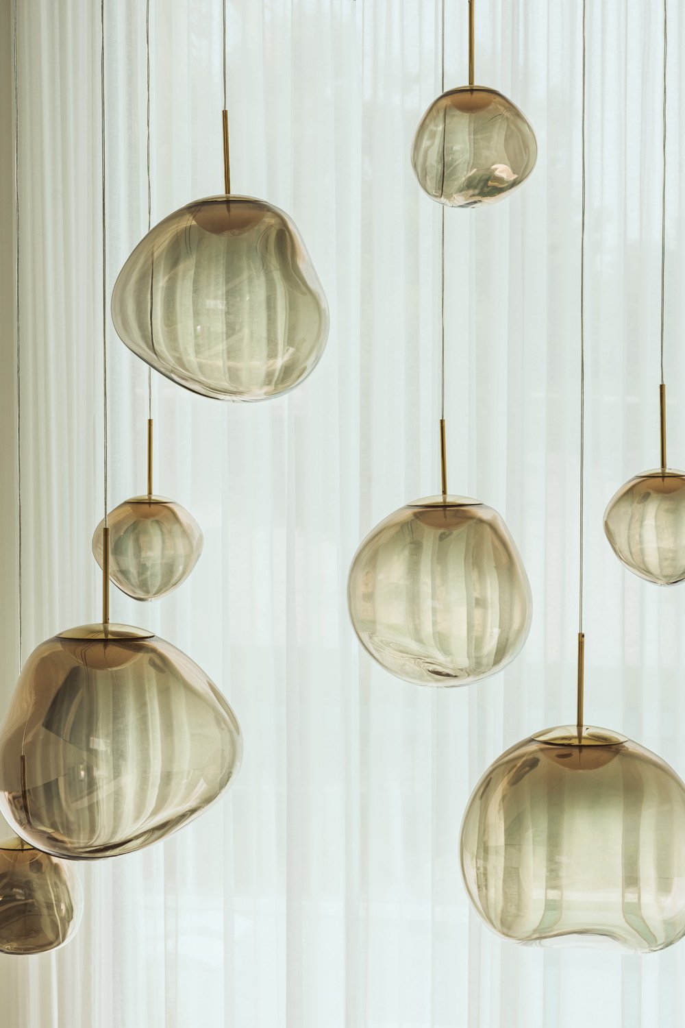 Cluster of smoked glass pendants against sheer curtains in the double-height living room of Villa Ambra, Dubai.