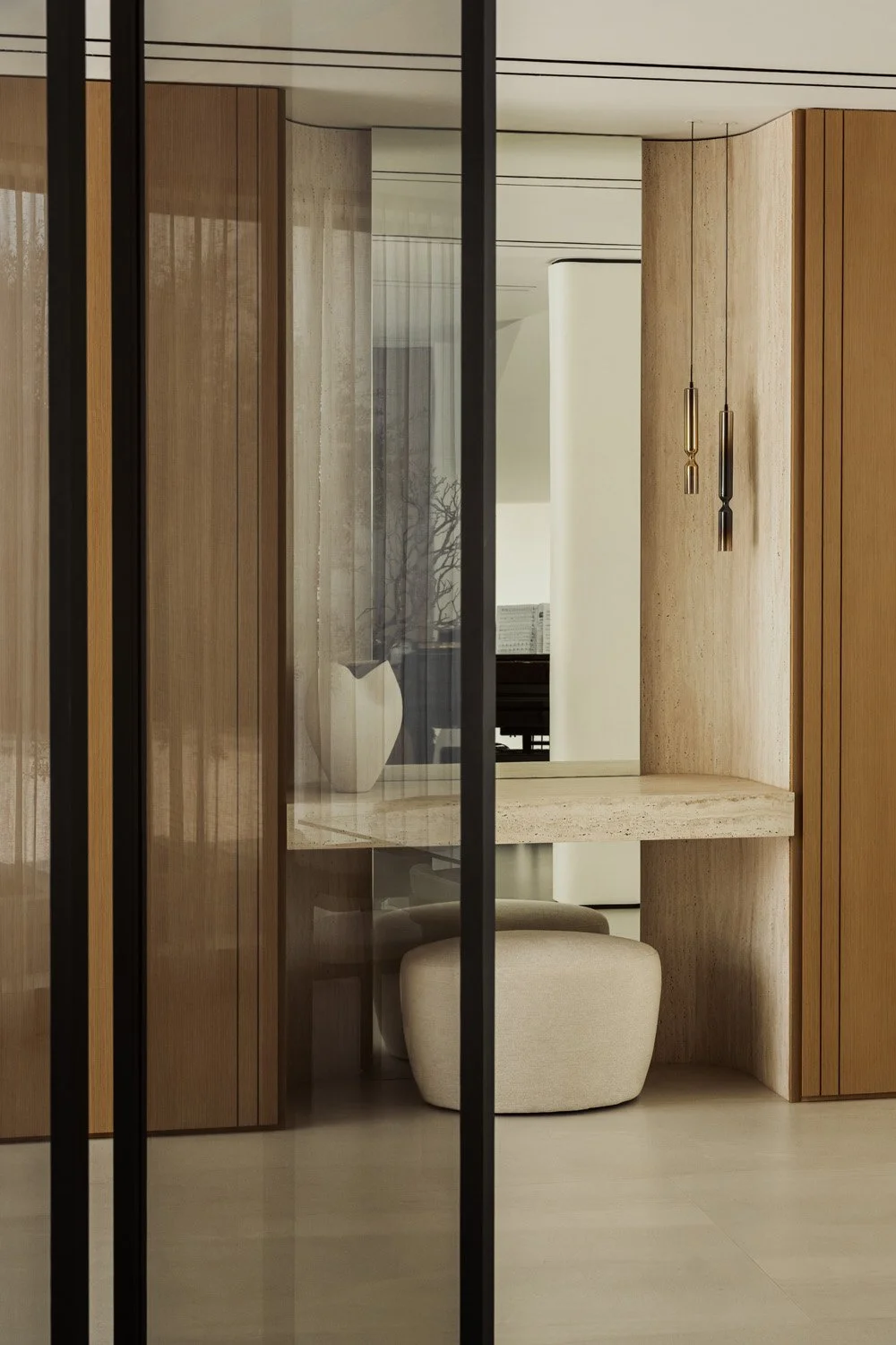 The travertine entrance console of Villa Ambra seen through a mesh-glass screen, with a curved travertine niche, glass pendants and an upholstered pouf.