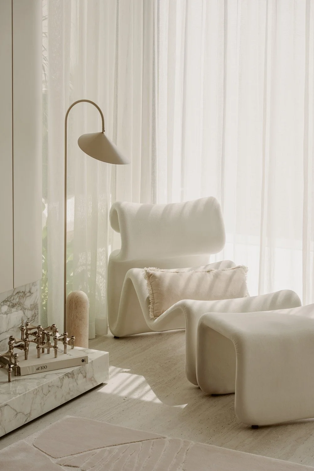lose-up of a sculptural organic-form bouclé Etcetera lounge chair and ottoman with a brass arc floor lamp, marble side surface, and sheer floor-to-ceiling curtains, in a luxury living room designed by Limestone in Arabian Ranches Dubai
