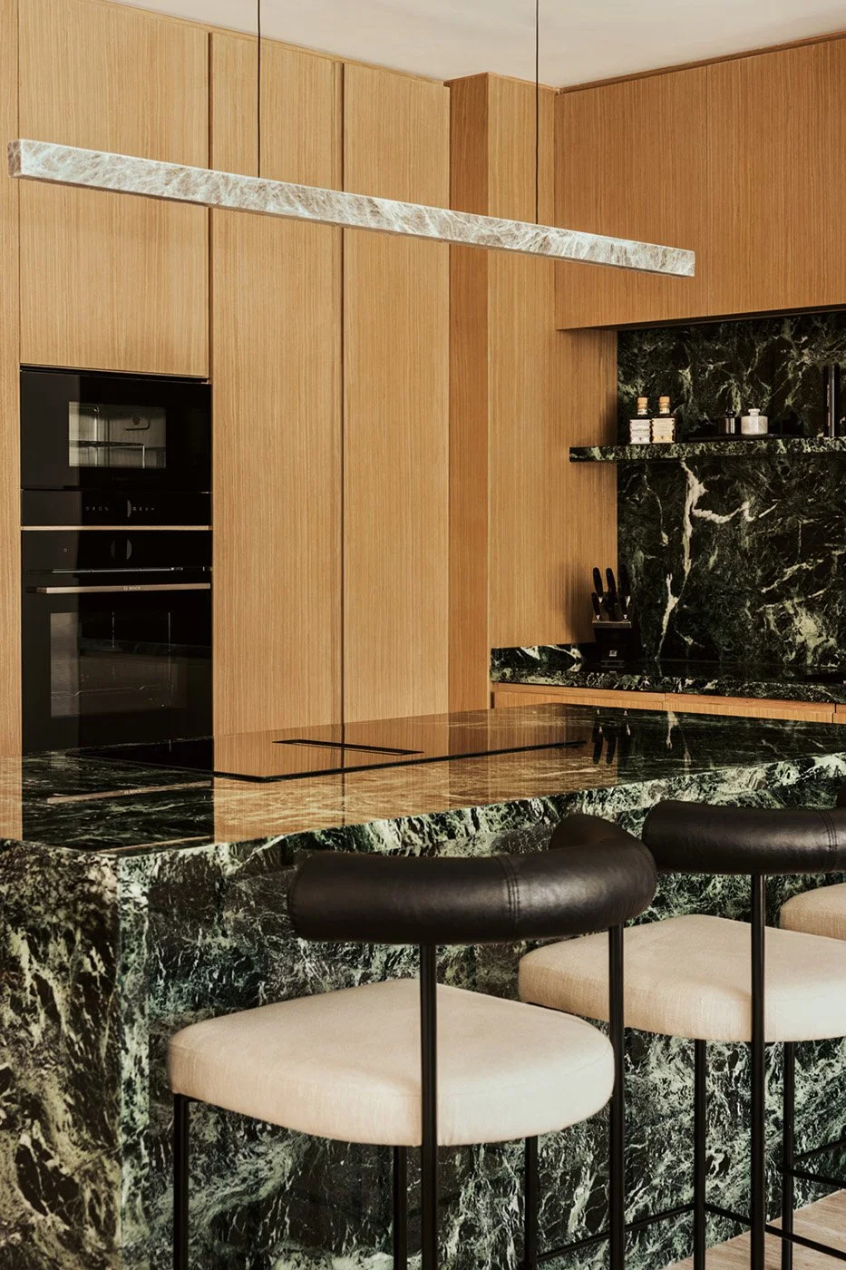 Close-up of a bespoke kitchen with green marble backsplash, integrated oak cabinetry, and black appliances designed by Limestone