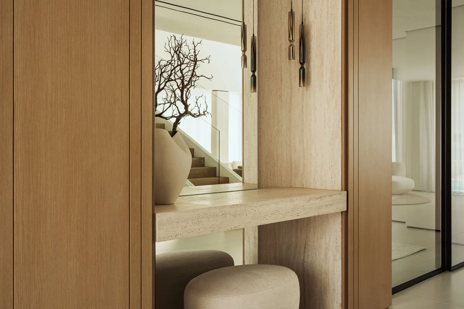 Entrance console niche in Villa Ambra, Jumeirah Islands, lined in natural travertine, with oak panelling and a mirror reflecting the oak staircase.