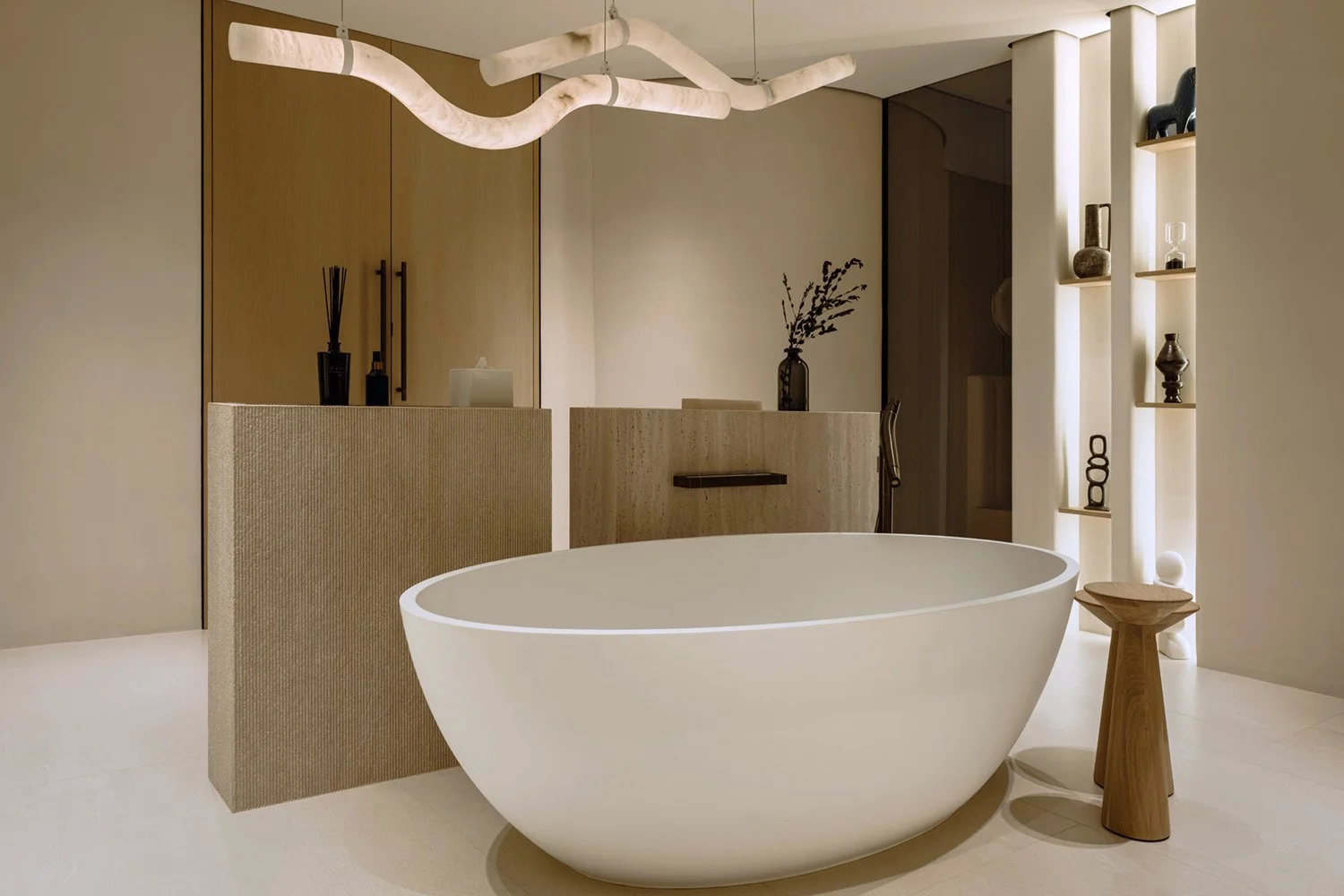 Master bathroom in Villa Ambra, Jumeirah Islands, with a freestanding bathtub, his-and-hers stone pedestals in two textures, an alabaster pendant and lit niche shelving.