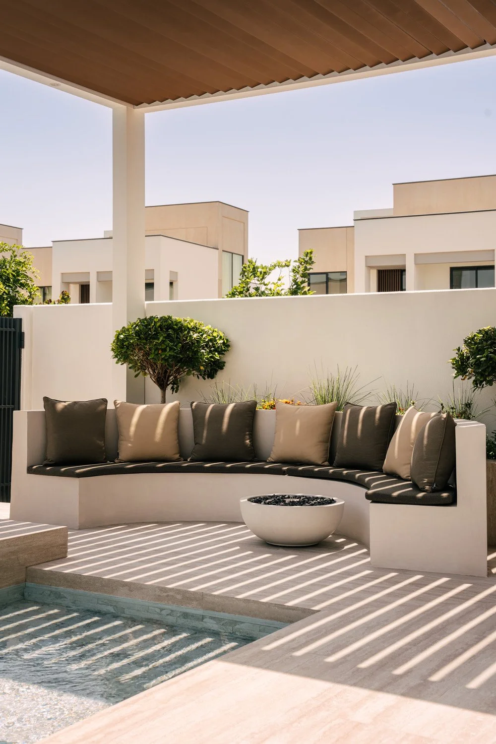 Luxury outdoor lounge with a timber pergola, curved built-in seating, manicured topiary, and a concrete fire bowl, designed by Limestone in Dubai