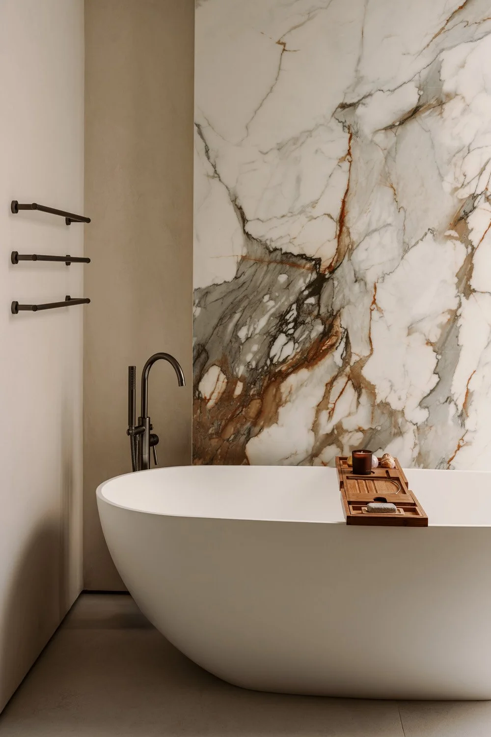 Luxury bathroom with a freestanding oval bathtub, dramatic Calacatta marble feature wall, and matte black floor-mounted faucet by Limestone