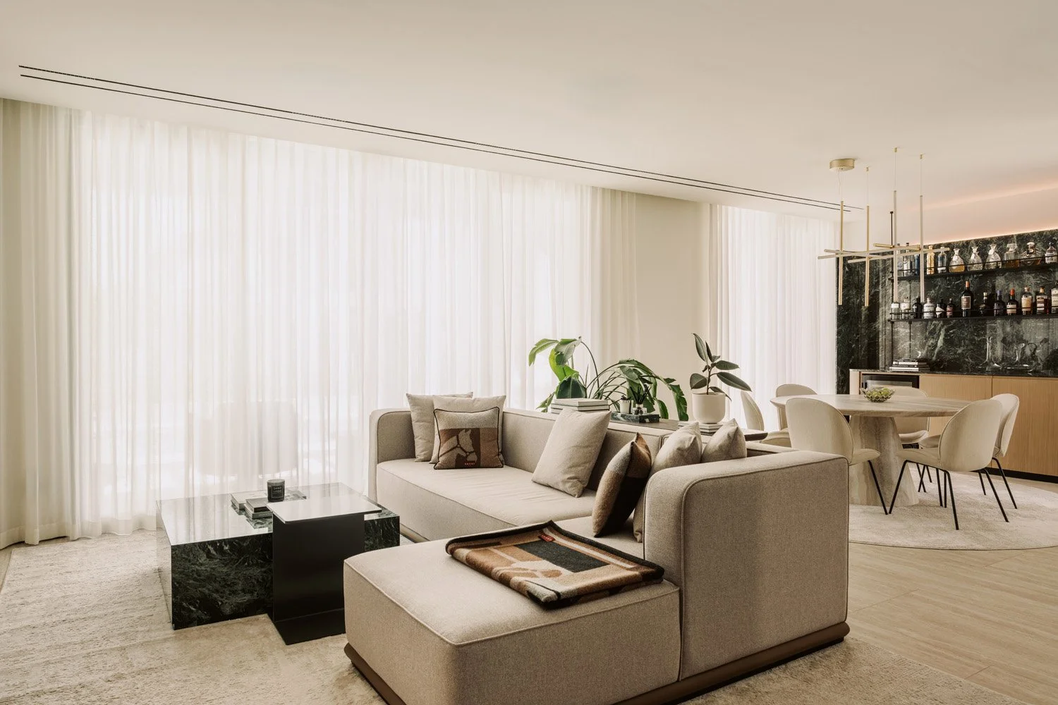 Expansive open-plan living and dining room with neutral upholstery, green marble coffee table, and a bespoke bar wall designed by Limestone