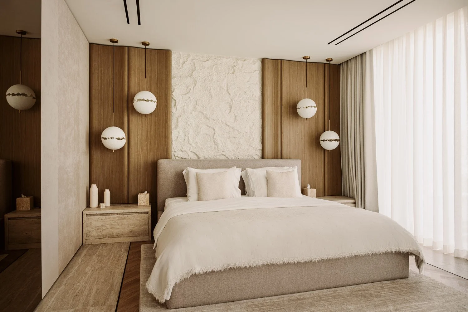 Luxury master bedroom with vertical oak wall panelling, a sculptural raw stone artwork feature, globe pendant lights with brass fittings, and a linen upholstered bed by Limestone