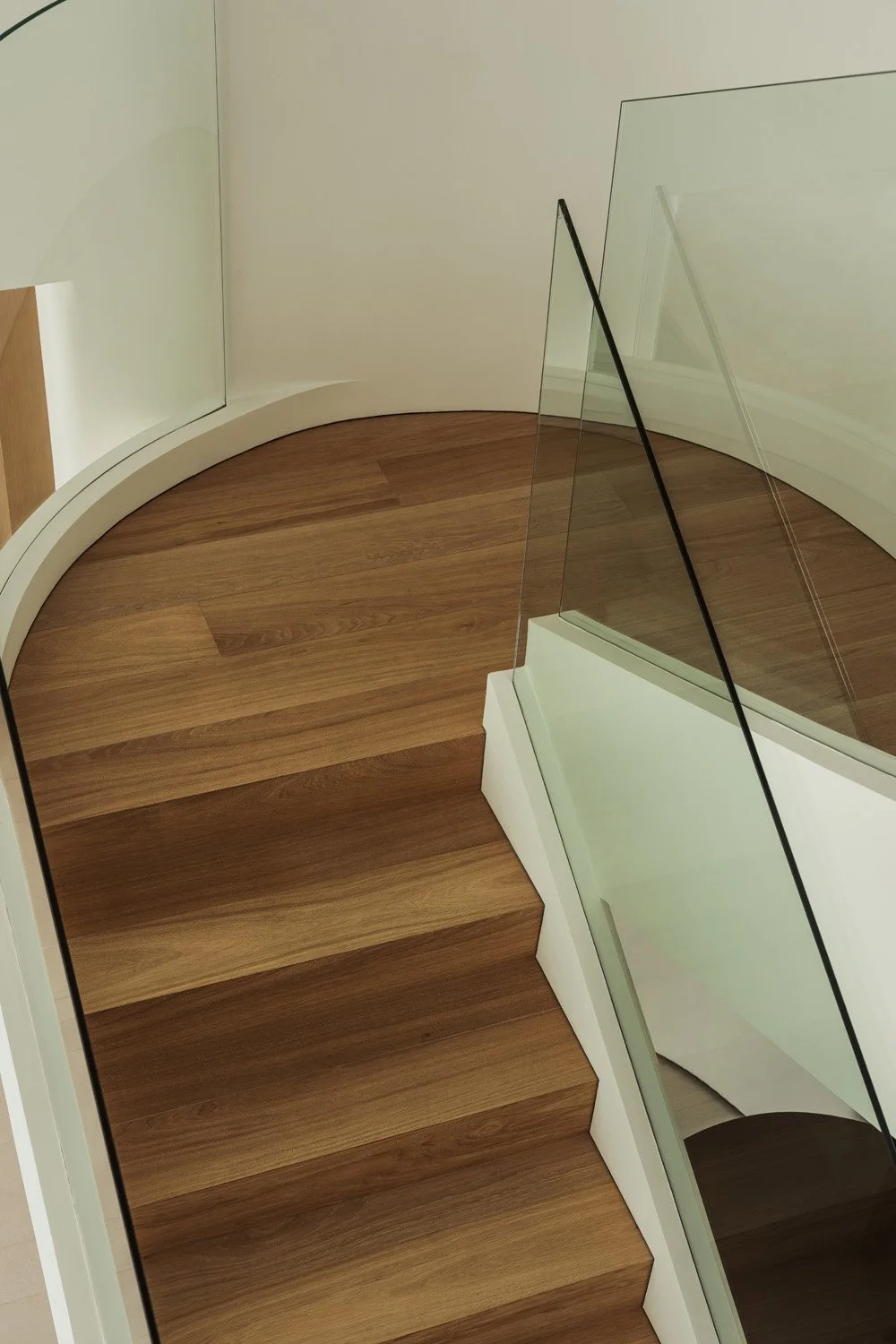 Oak staircase with a curved landing and frameless glass balustrade, seen from above, in Villa Ambra, Jumeirah Islands, Dubai.