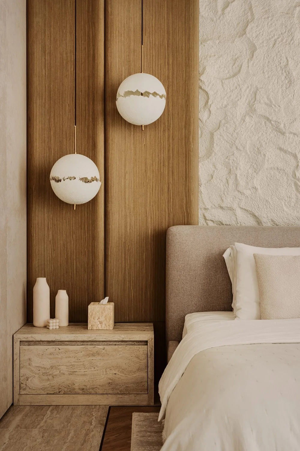 Luxury bedroom bedside vignette with stacked globe pendant lights, vertical oak panelling, travertine nightstand, and sculptural raw stone wall detail by Limestone