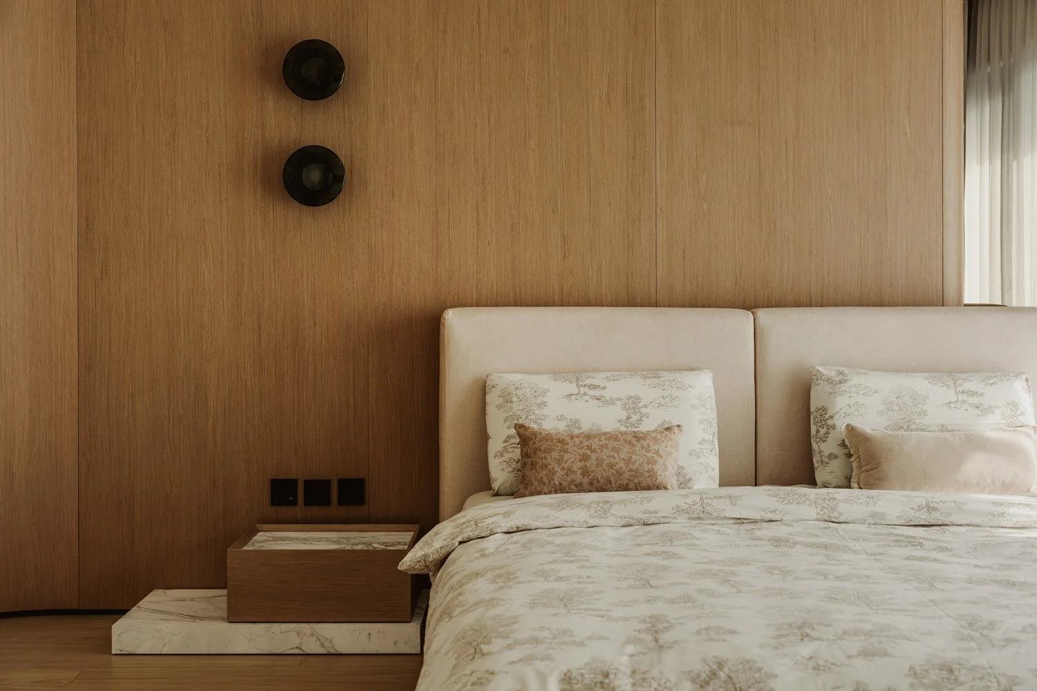Full view of a luxury master bedroom with a floor-to-ceiling oak veneer feature wall, tufted linen headboard, toile de Jouy bedding, floating marble nightstand, and smoked glass wall sconces, designed by Limestone in Dubai