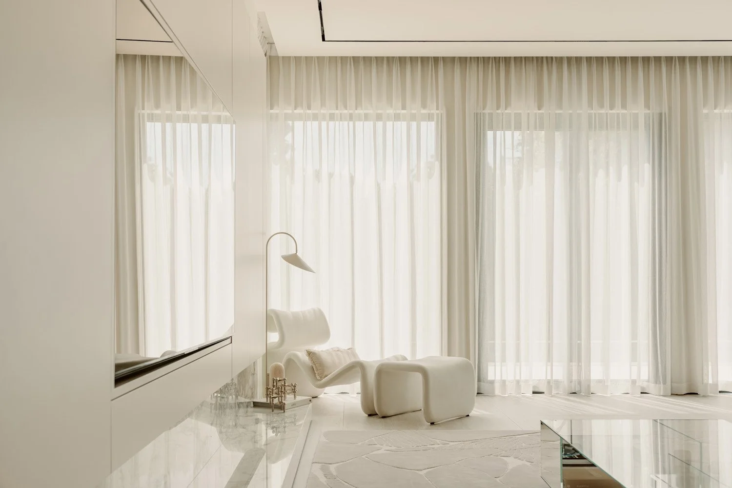 All-white luxury living space with a sculptural organic-form Etcetera Lounge chair and ottoman, floor-to-ceiling sheer curtains, and a polished marble surface, designed by Limestone in Dubai
