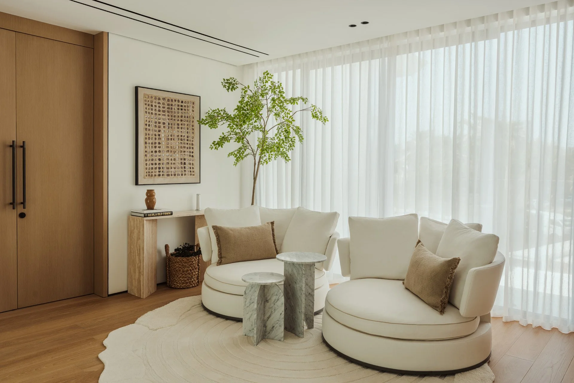 First-floor lounge in Villa Ambra with two round cream swivel armchairs, marble side tables, a travertine console, framed artwork and oak double doors to the master suite.