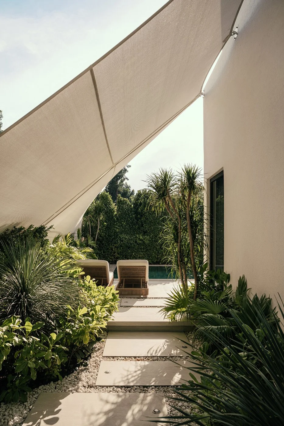 Luxury villa garden pathway with architectural sail shade, stepping stone path, pebble ground cover, and dense tropical planting leading to a pool terrace, designed by Limestone in Dubai