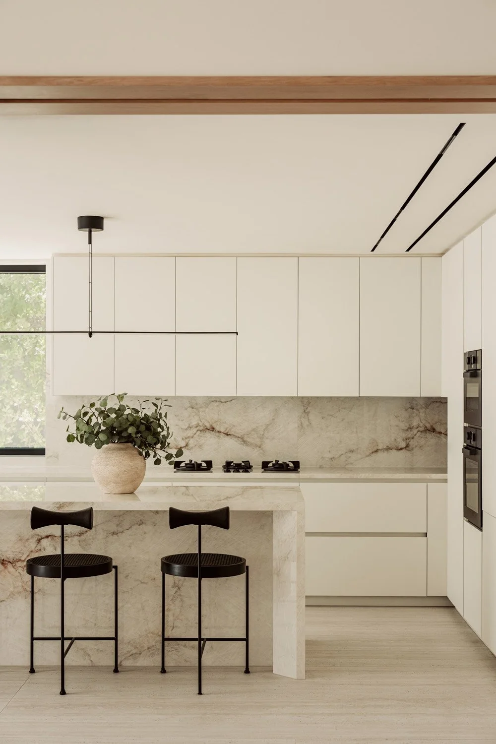Luxury kitchen designed by Limestone Dubai featuring a Calacatta marble island, sculptural black bar stools, white handleless cabinetry, and a marble stone backsplash with garden views