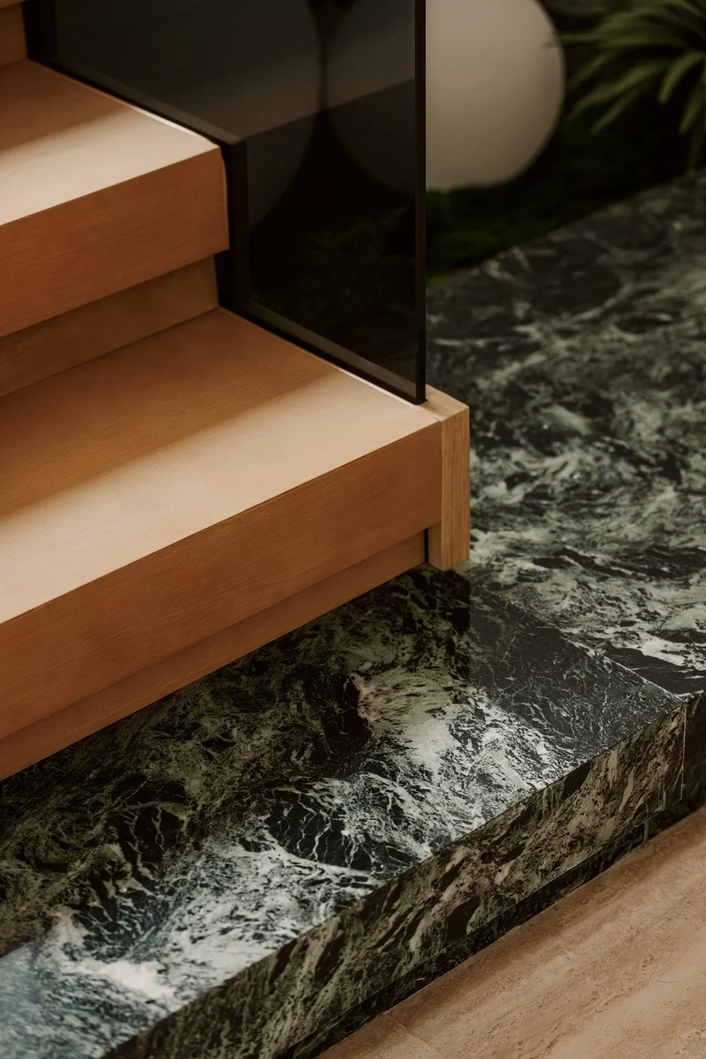 Architectural detail of a bespoke staircase with Alpi Verde marble base, oak timber treads, and smoked glass balustrade by Limestone