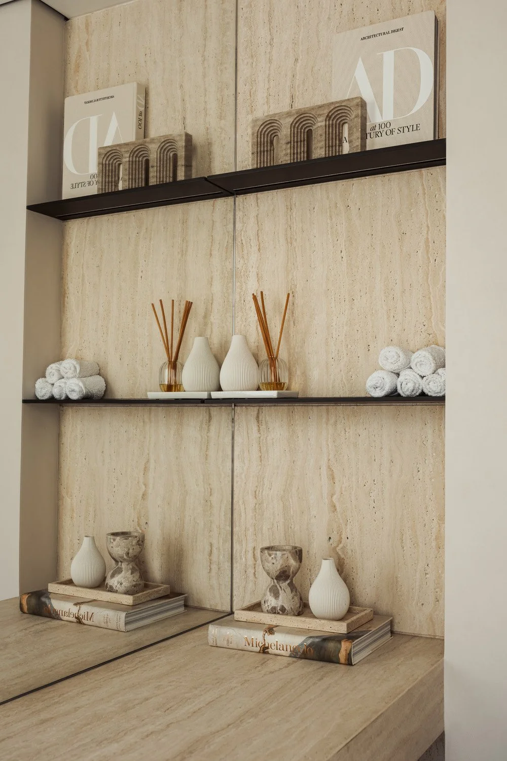 Natural travertine wall with slim dark metal shelves and a travertine counter in the powder room of Villa Ambra, Jumeirah Islands, Dubai.