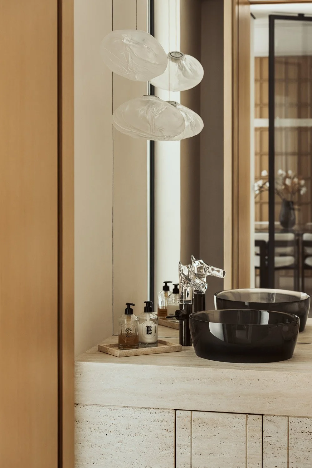 Carved travertine vanity with a smoked-glass basin, a sculptural glass-spout tap and hand-blown glass pendants in the powder room of Villa Ambra, Dubai.