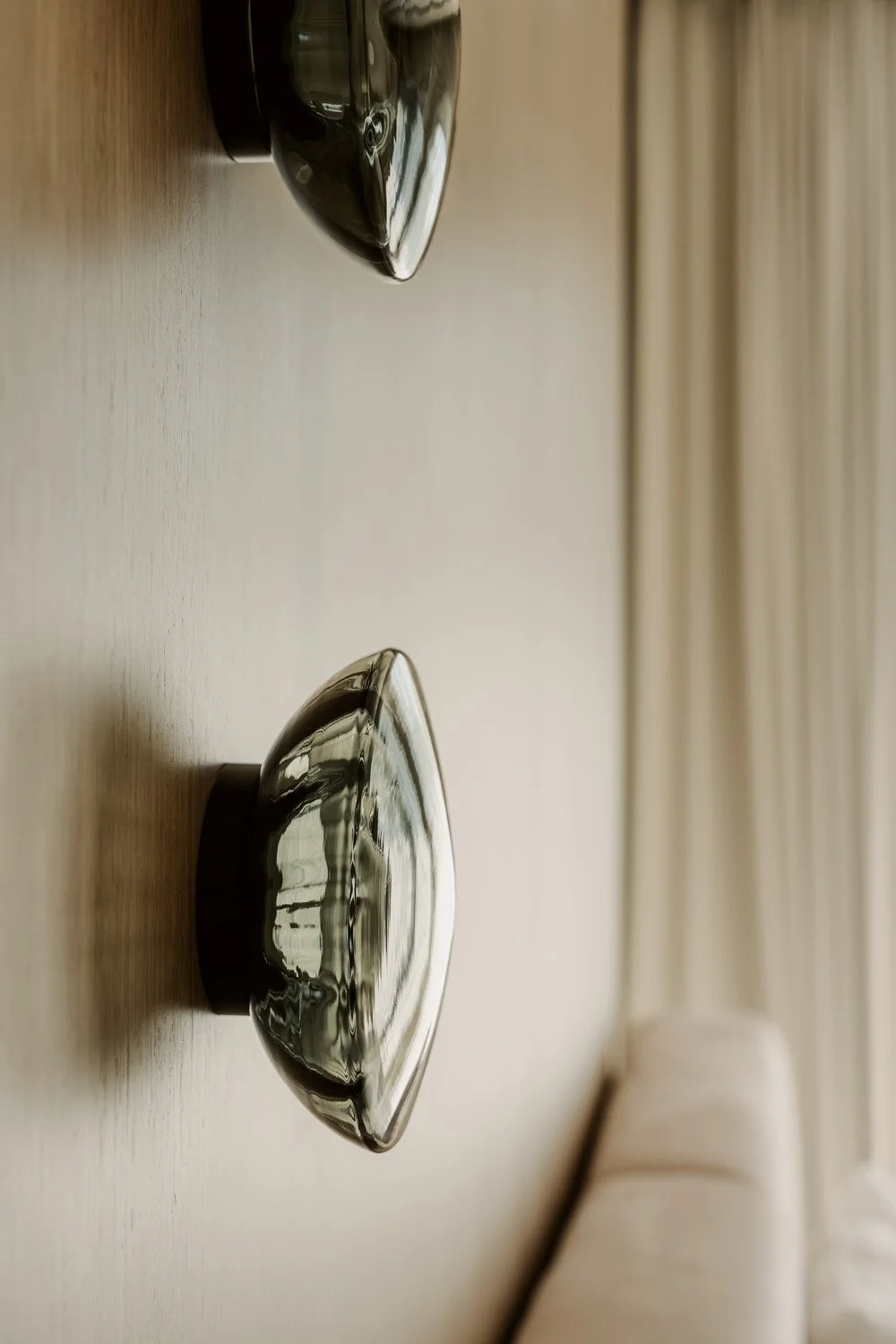 Close-up detail of a sculptural smoked glass dome wall sconce mounted on an oak veneer panel in a luxury master bedroom designed by Limestone in Dubai