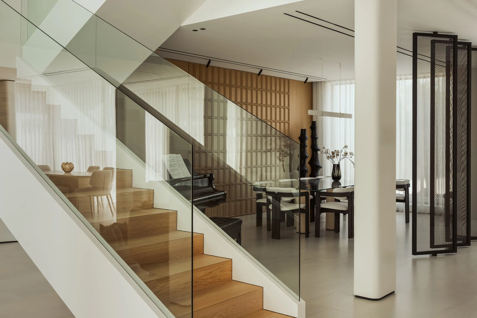 Oak staircase with a frameless glass balustrade in Villa Ambra, Jumeirah Islands, looking through to the grand piano, the dining room and mesh-glass screens.