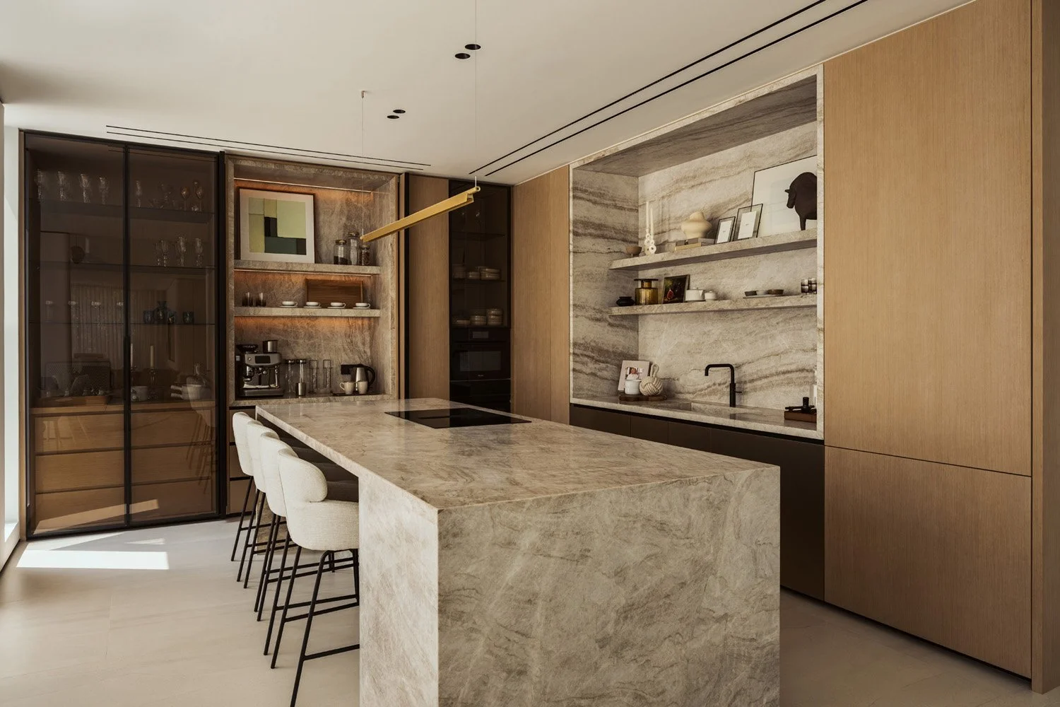 Kitchen in Villa Ambra, Jumeirah Islands, Dubai, with a Taj Mahal quartzite island and cream bar stools, smoked-glass display cabinets, the lit coffee station, oak joinery and a quartzite-framed sink alcove.
