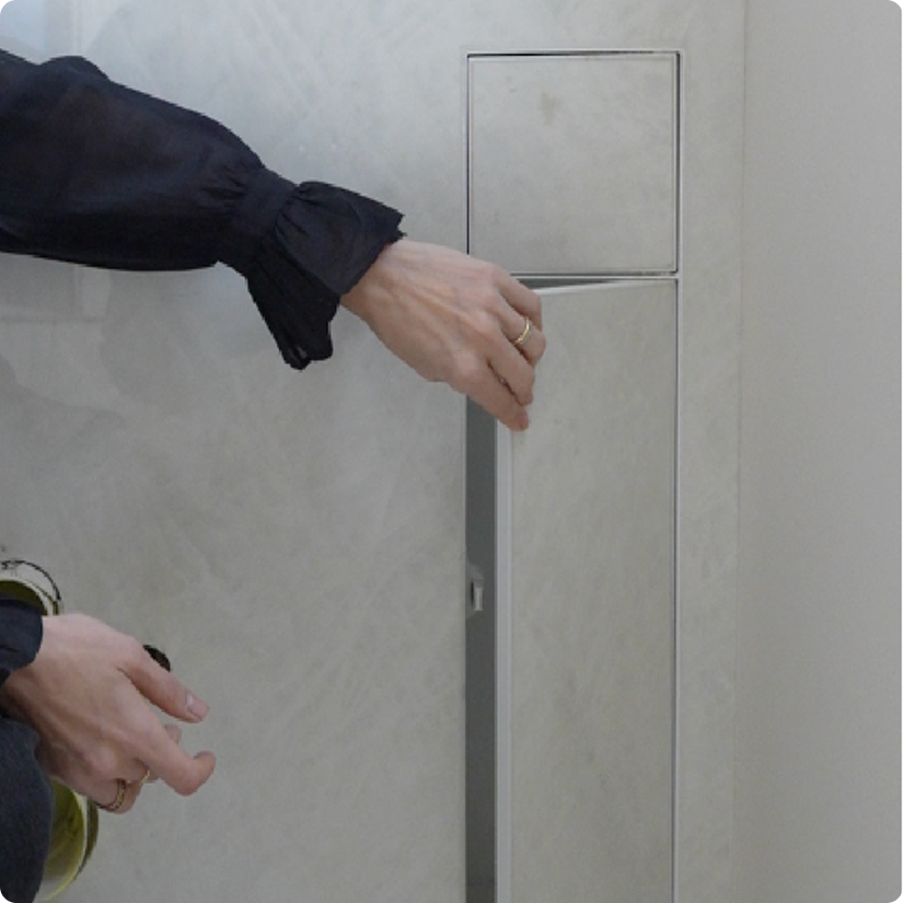 A person in a black long-sleeve shirt is opening a gray metal locker or cabinet, with their left hand on the door handle and right hand near the bottom of the door.