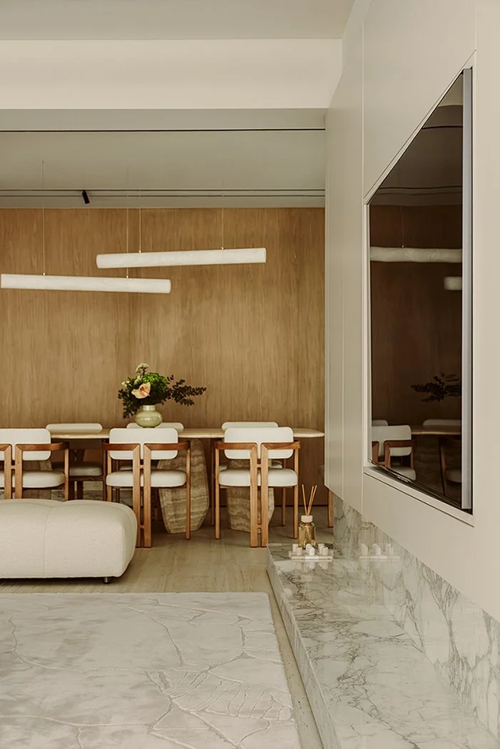 Luxury dining room with a full-height oak veneer feature wall, oval travertine pedestal table, timber dining chairs, and sculptural white tube pendant lights, seen from the living room, designed by Limestone in Dubai