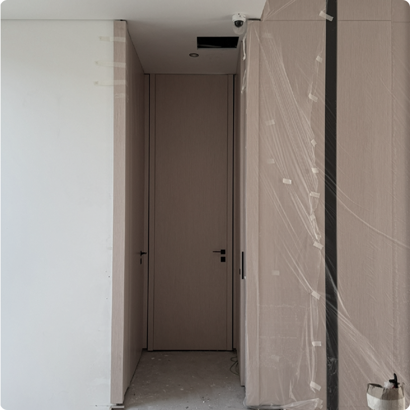 Hallway with closed wooden doors at the end, construction area with plastic covering on the right side, and a security camera on the ceiling.