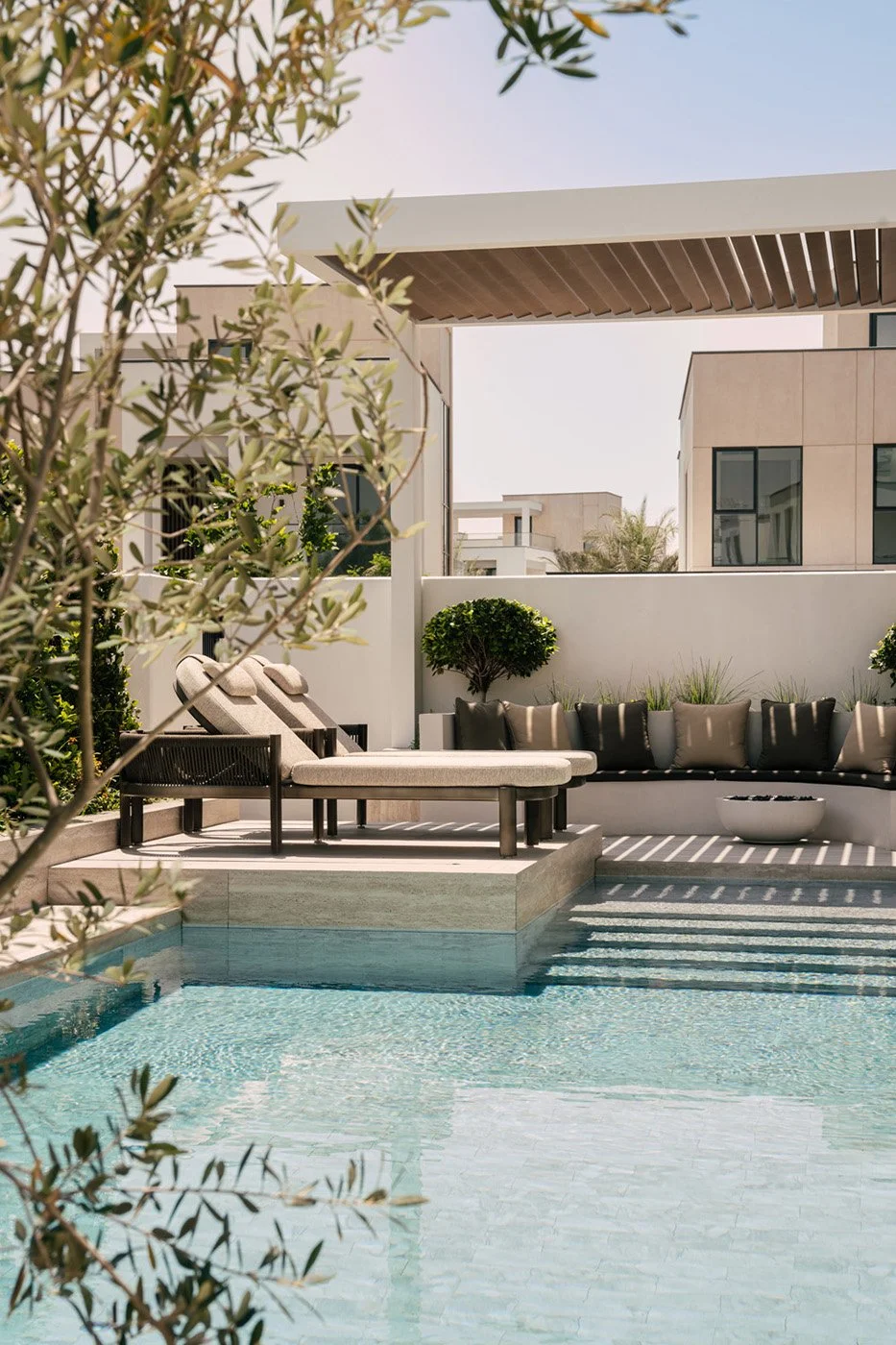 Luxury villa pool terrace with designer sun loungers, curved outdoor seating, topiary planters, and a timber louvred pergola designed by Limestone in Dubai