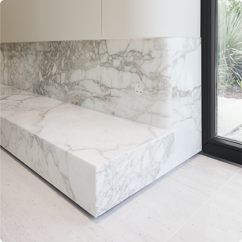 Marble bench built into a marble wall next to a glass door in a modern, minimalist interior.