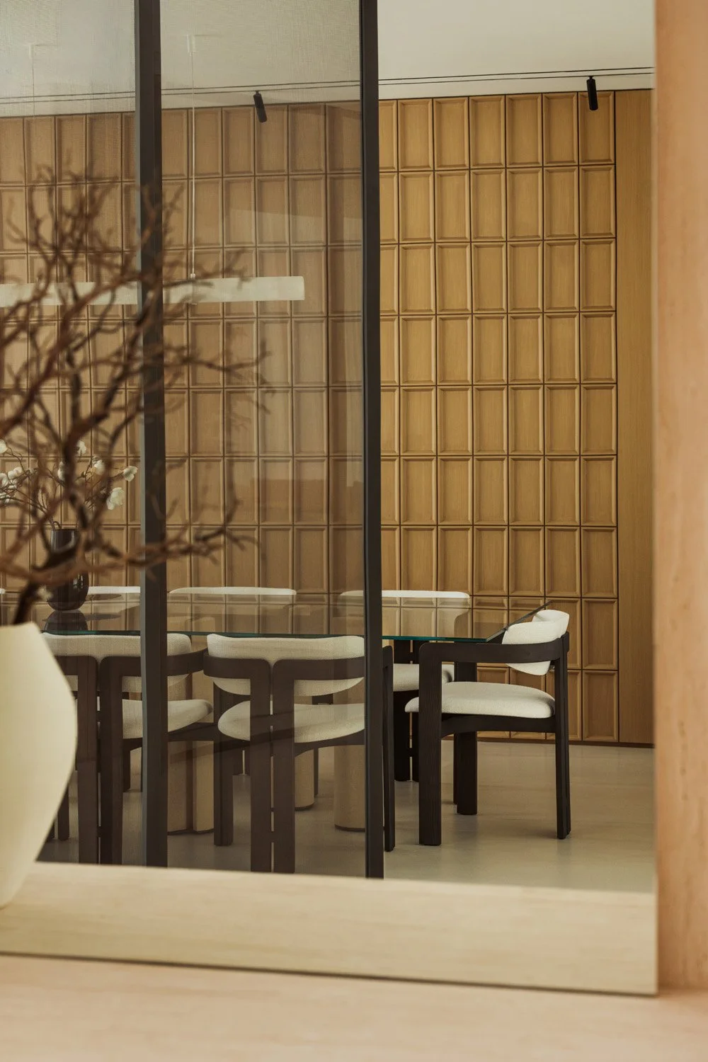 The oak-panelled dining room of Villa Ambra seen through the entrance mesh-glass screen, reflected in the travertine-framed console mirror.