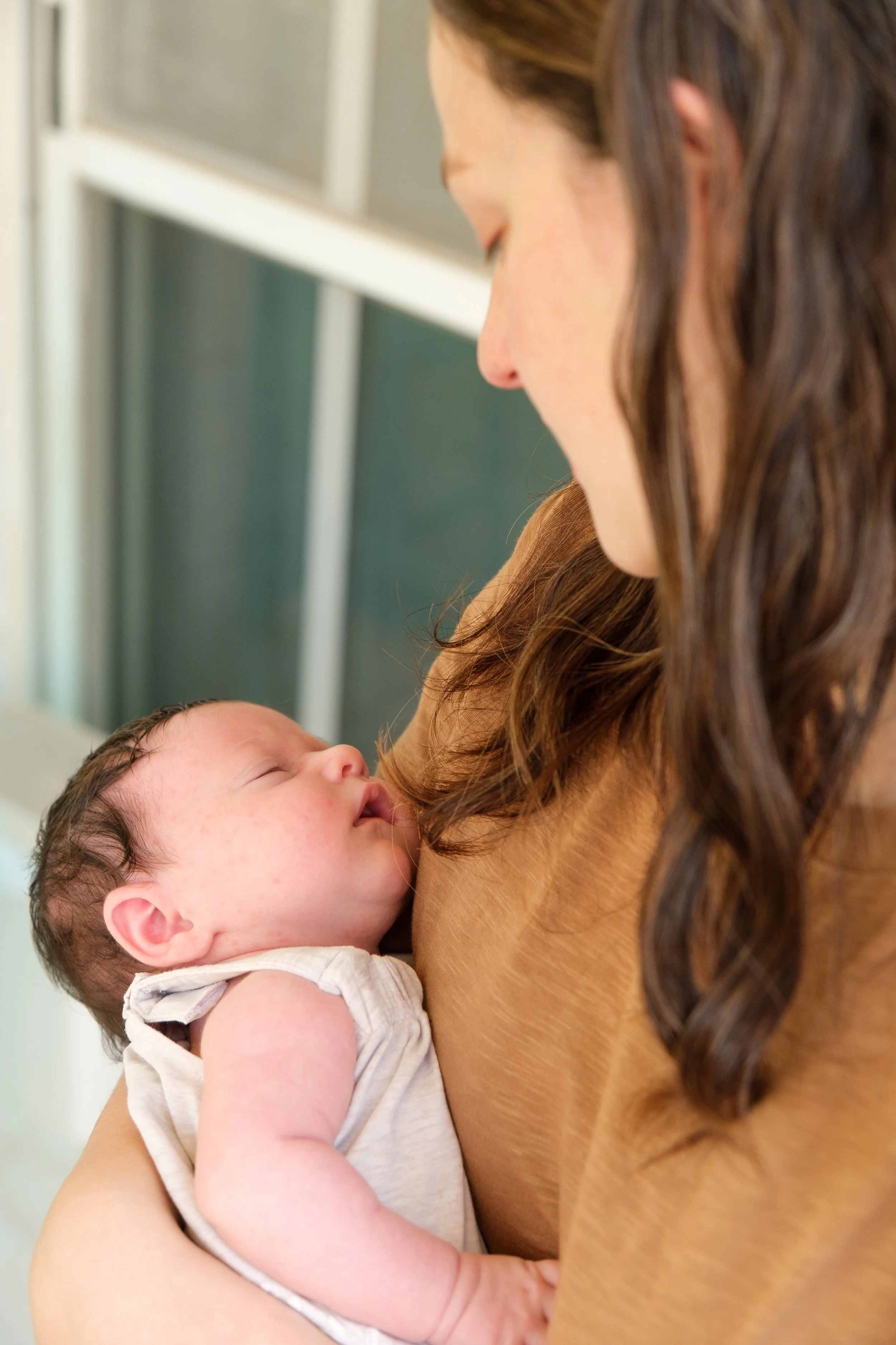 A woman holding a sleeping baby close to her chest, with her face turned downward and her long wavy hair visible.