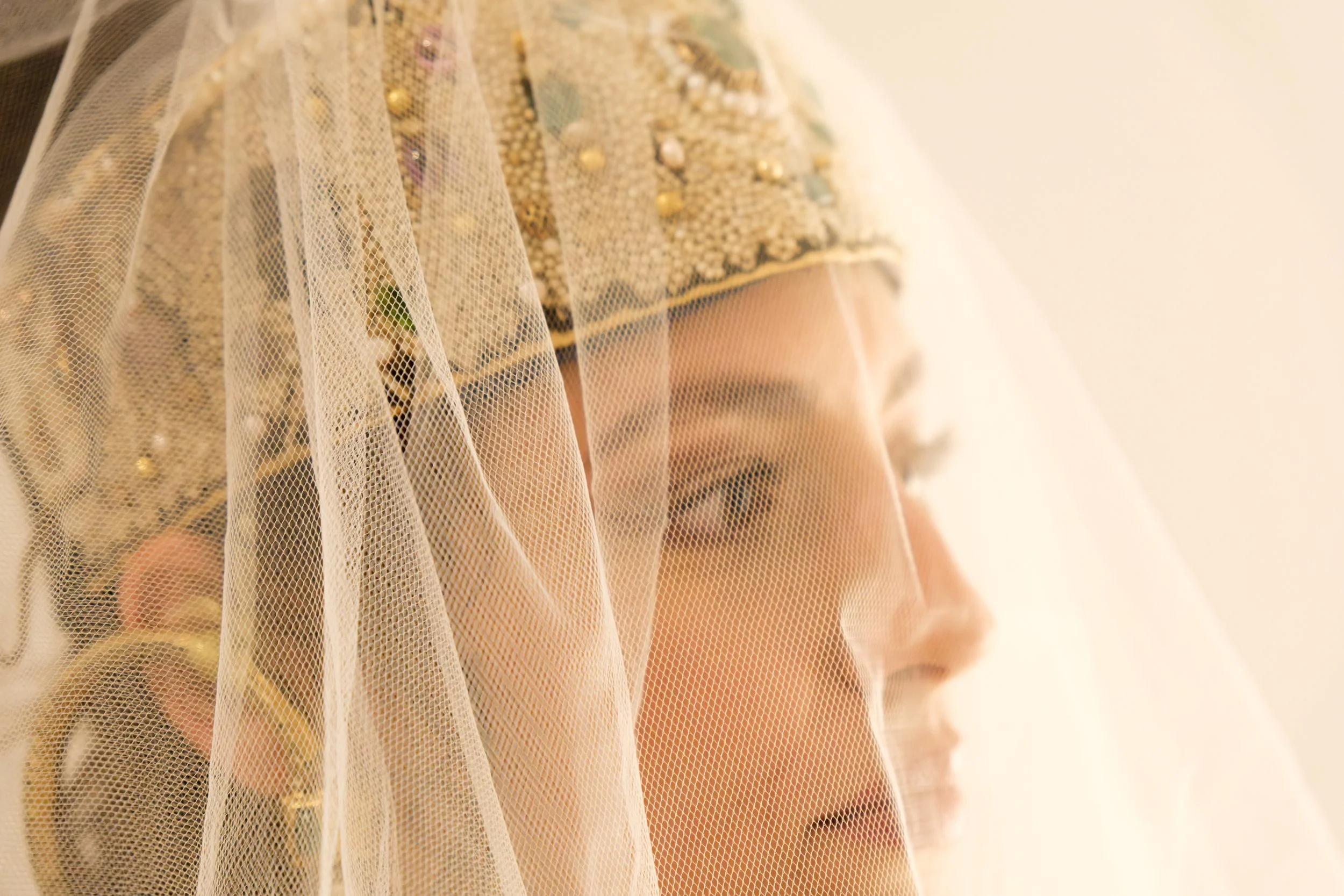 Close-up of a person wearing a gold, jeweled garment with a sheer tulle veil covering their face and shoulders.