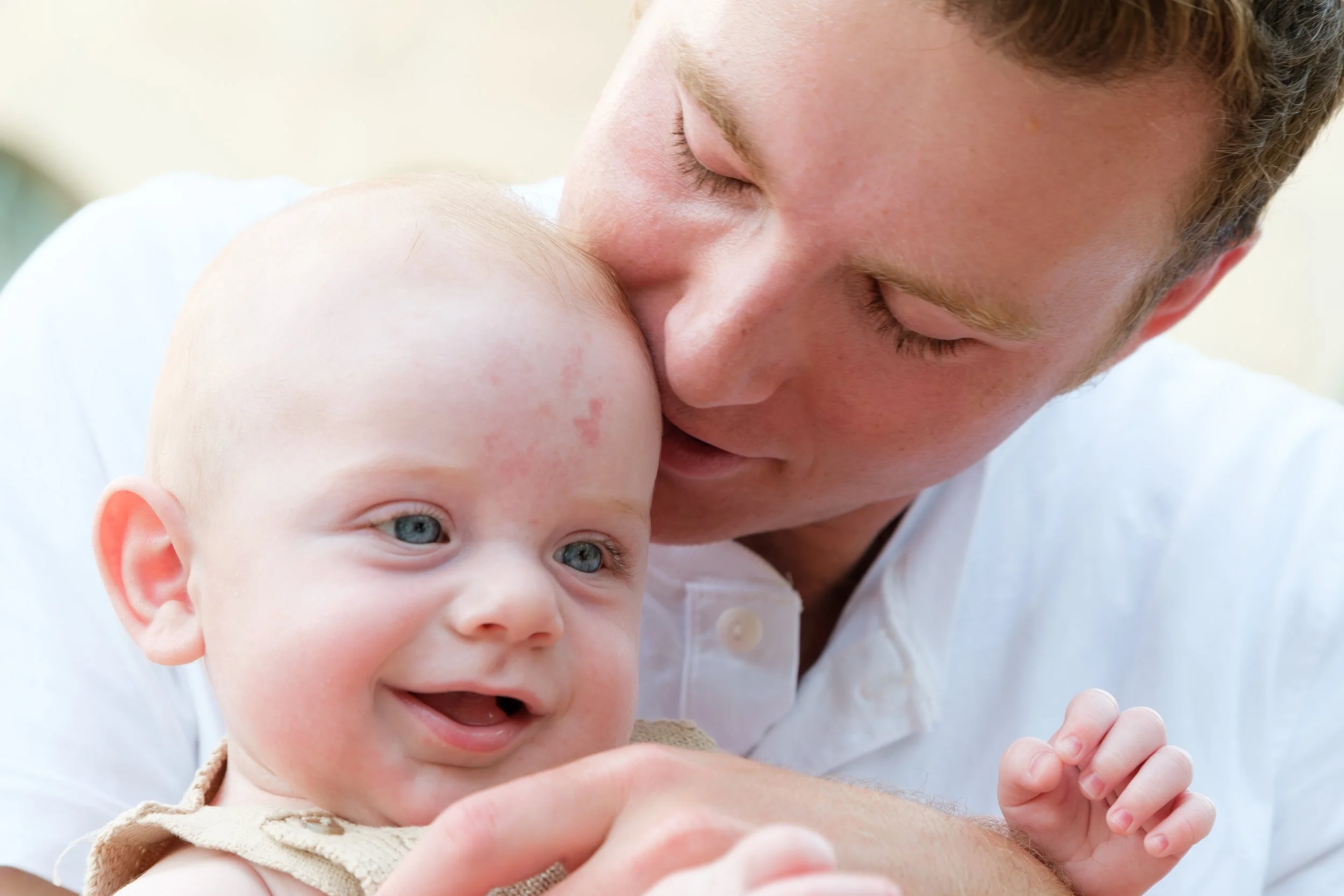 A man gently kisses a baby's head, showing an affectionate moment between them.