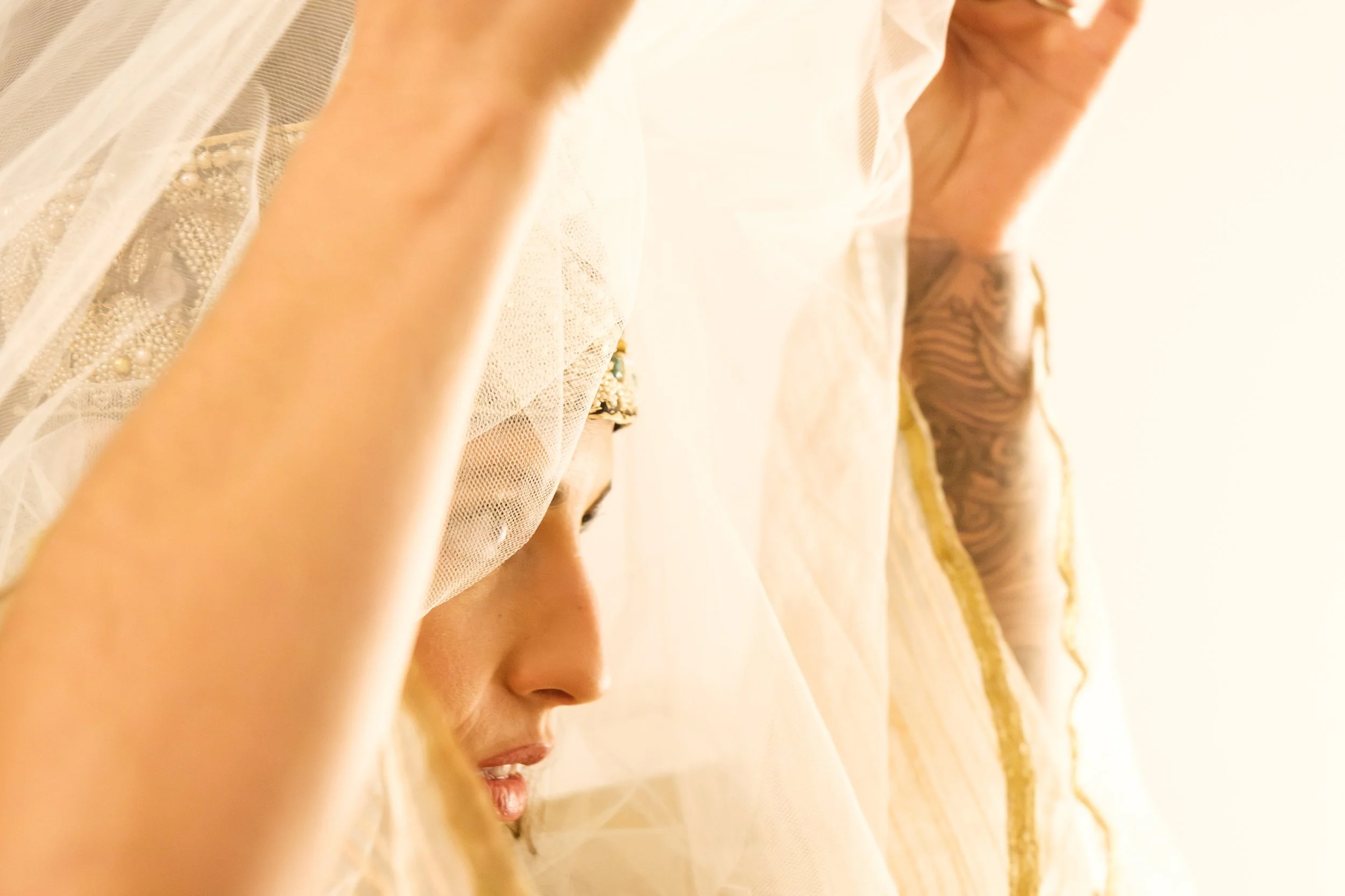 Close-up of a person's face, profile view, with a focus on the nose and lips, wearing a light-colored, delicate, possibly lace or sheer fabric garment, with blonde hair and ornate, detailed footwear visible in the background.