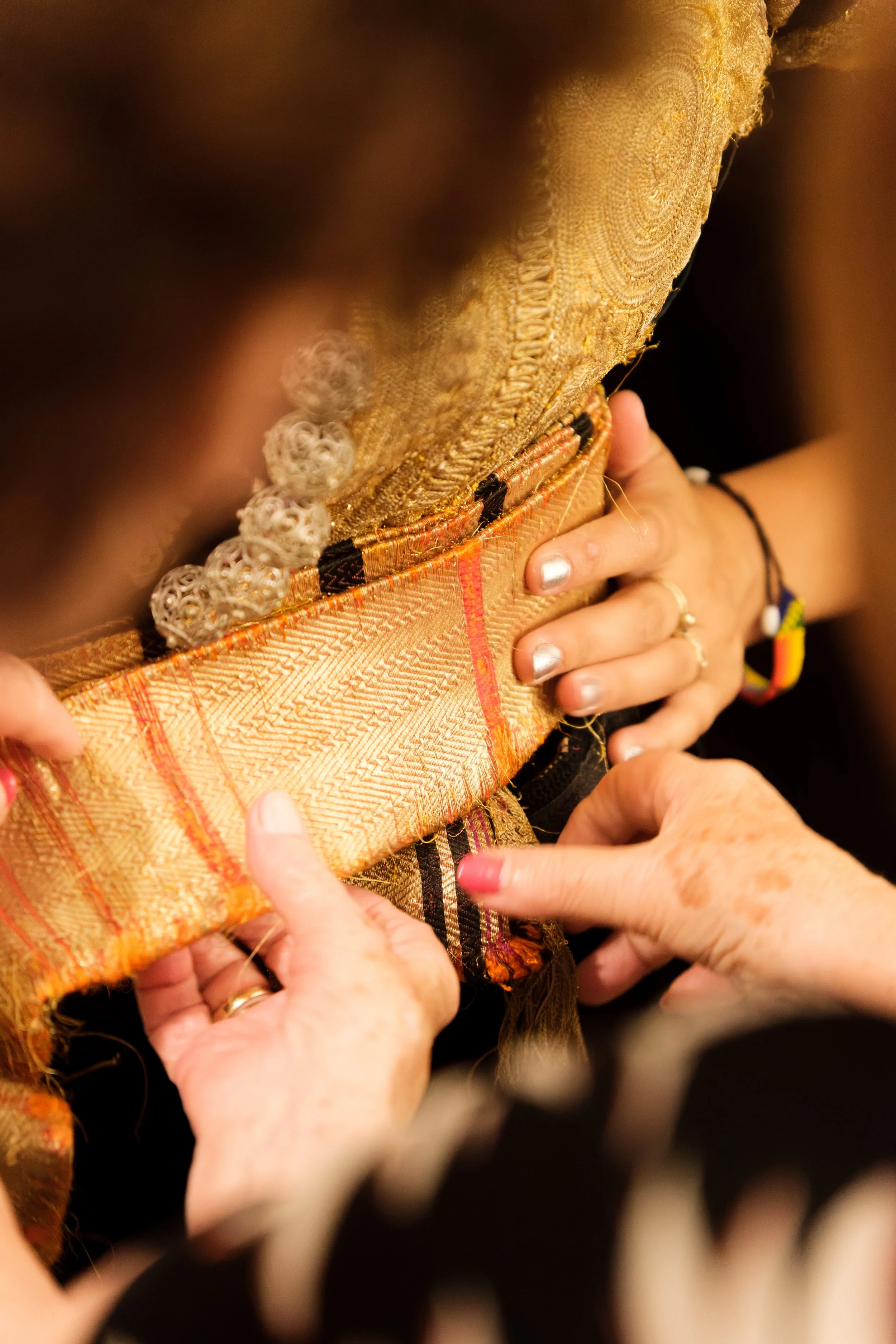 Close-up of hands adjusting traditional fabric on a wooden object, with intricate patterns and decorations, suggesting cultural or ceremonial significance.