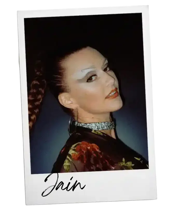 Een vrouwenportret met opvallende make-up en een glanzende ketting, met de naam 'Jain' onderaan.